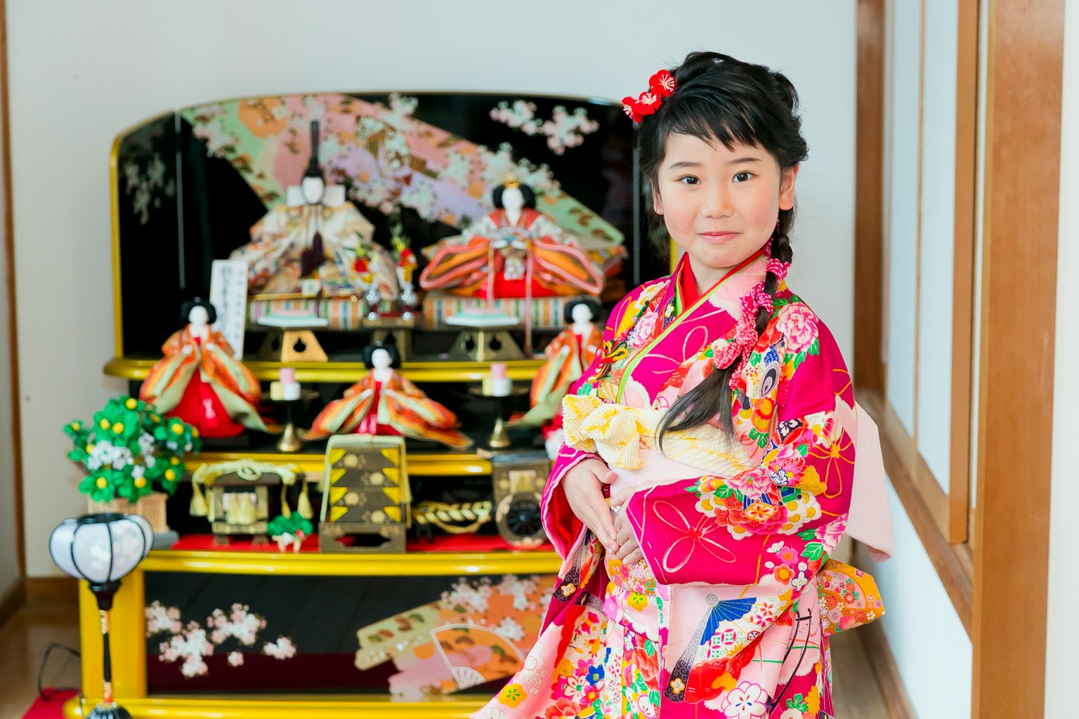 Một cô gái trong trang phục kimono đứng trước màn hình búp bê hina