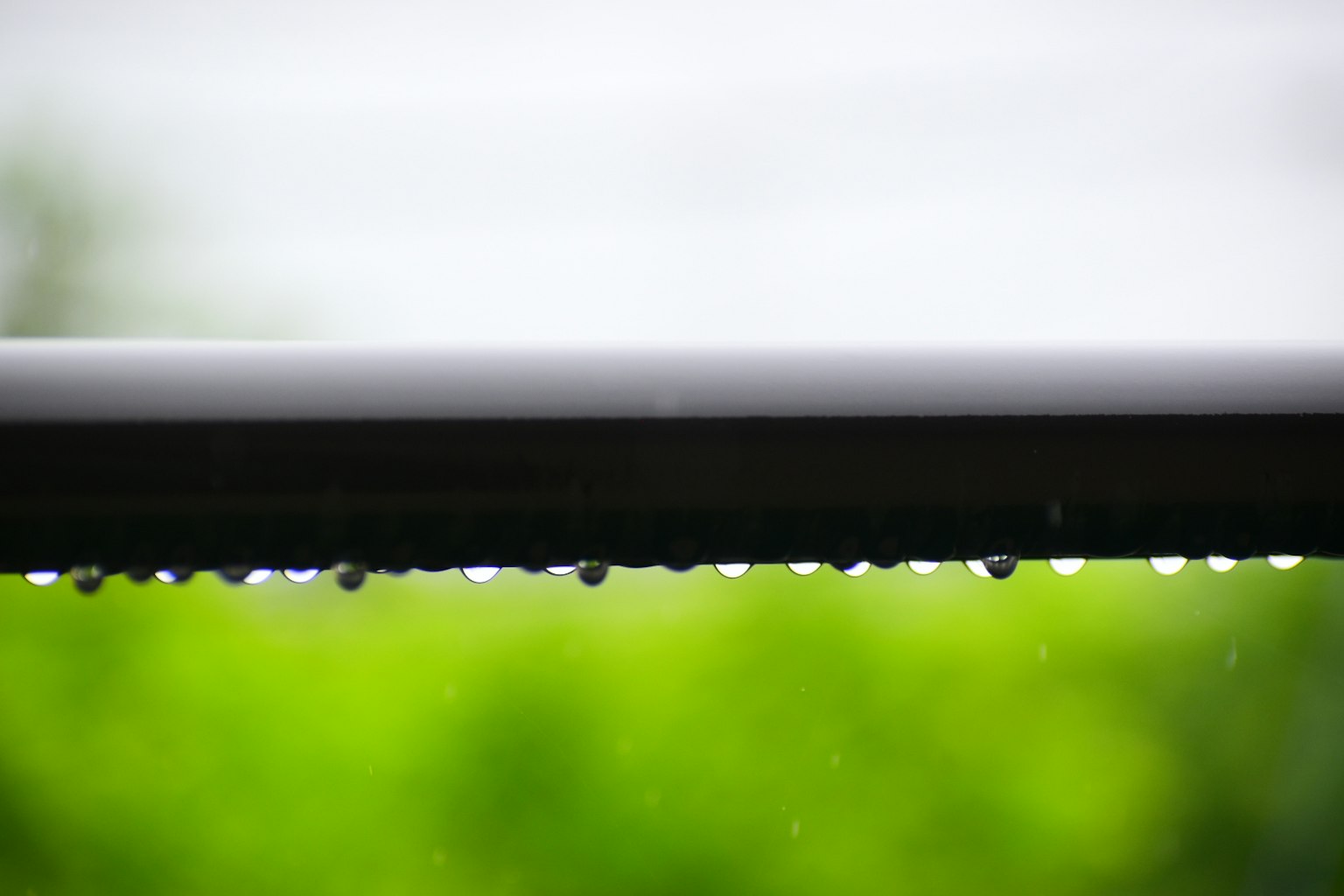 屋檐上的雨滴与模糊的绿色背景