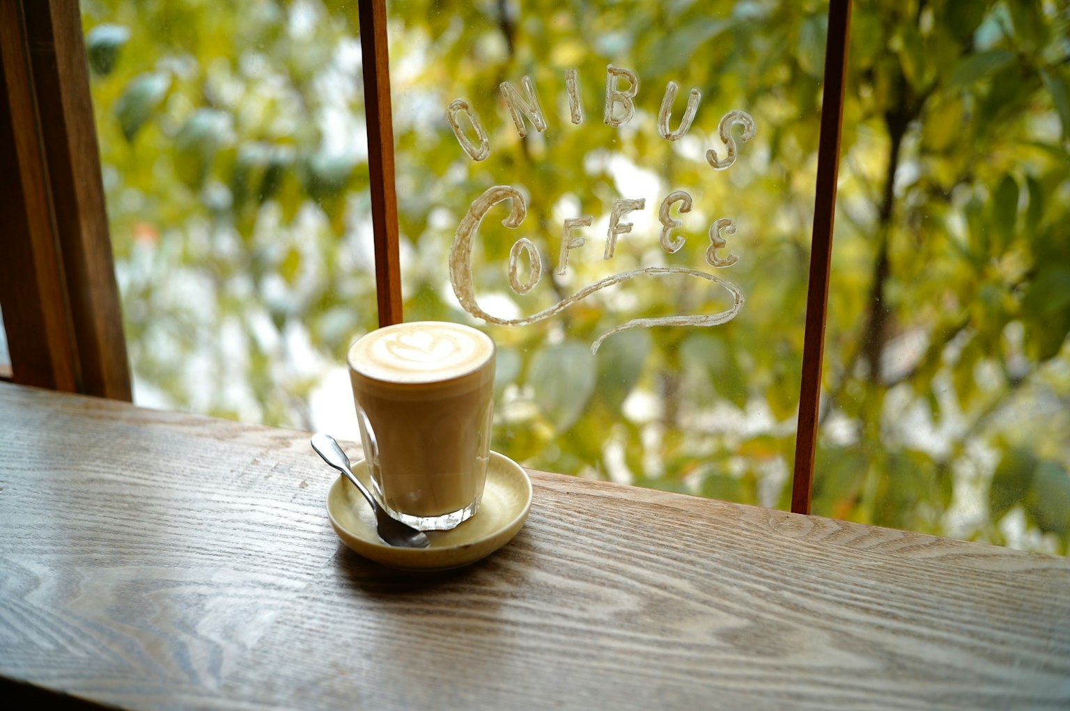 Café cremoso en una taza sobre un pequeño plato con una cuchara en un alféizar de madera