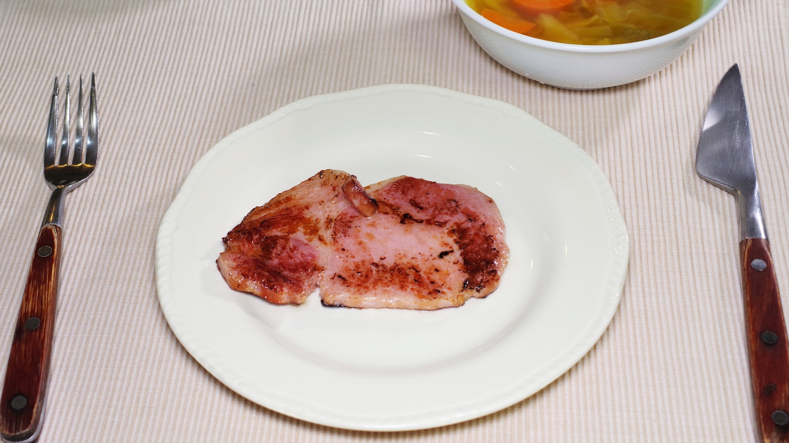 Một lát thịt chín trên đĩa với một bát súp ở phía sau
