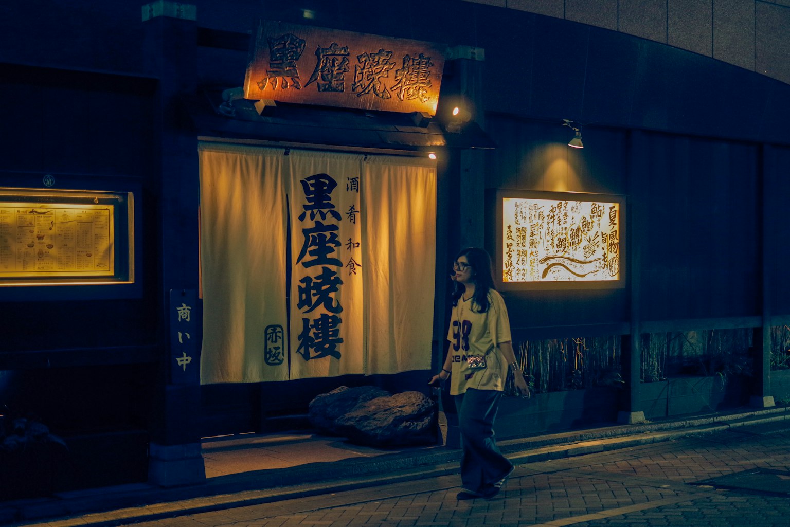 夜の街で歩く女性と和風の店の外観