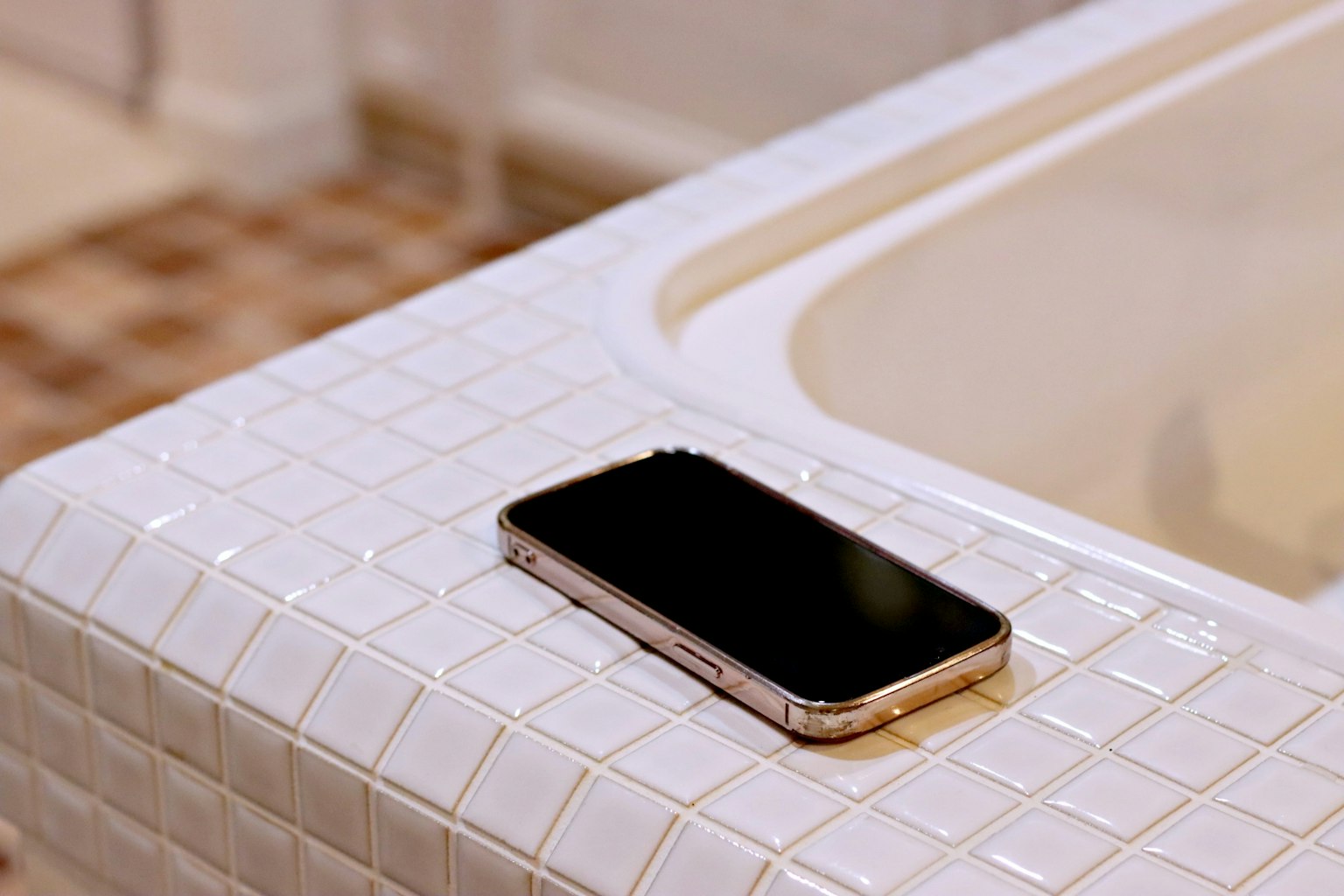 Smartphone negro colocado sobre una superficie de azulejos blancos en un baño