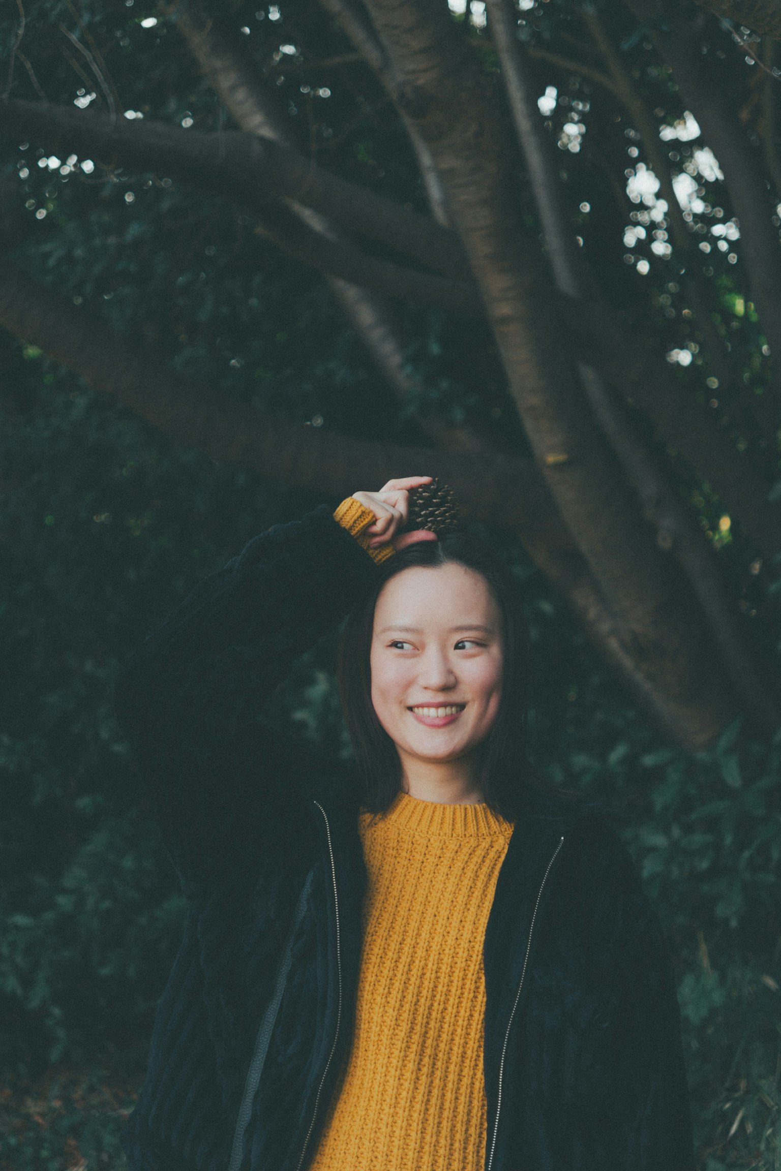 Smiling woman in a bright yellow sweater standing in front of a tree background