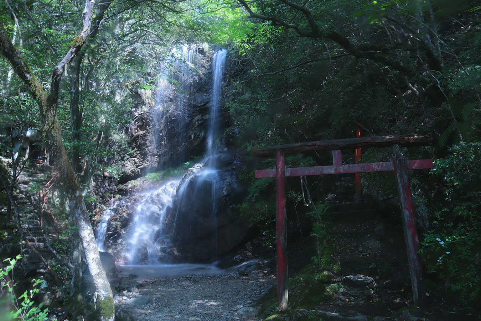A serene waterfall nestled in a lush forest with a traditional torii gate