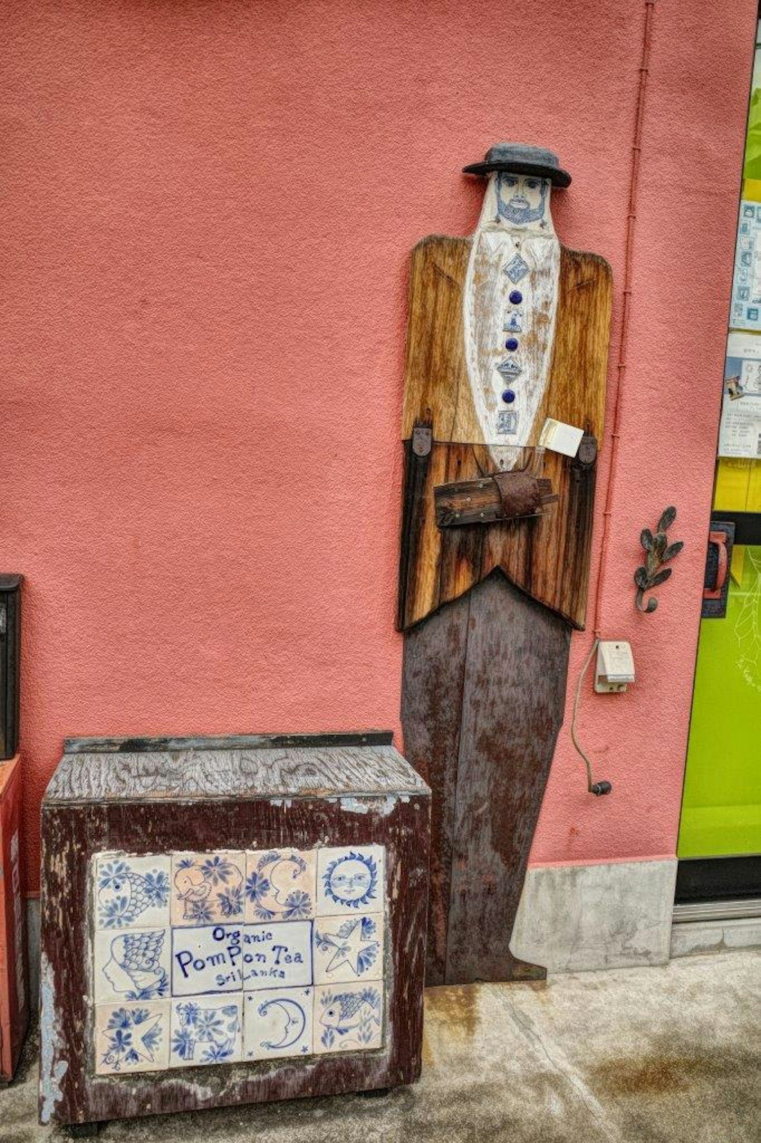 Figura in legno vestita da uomo contro un muro rosa con una scatola decorativa