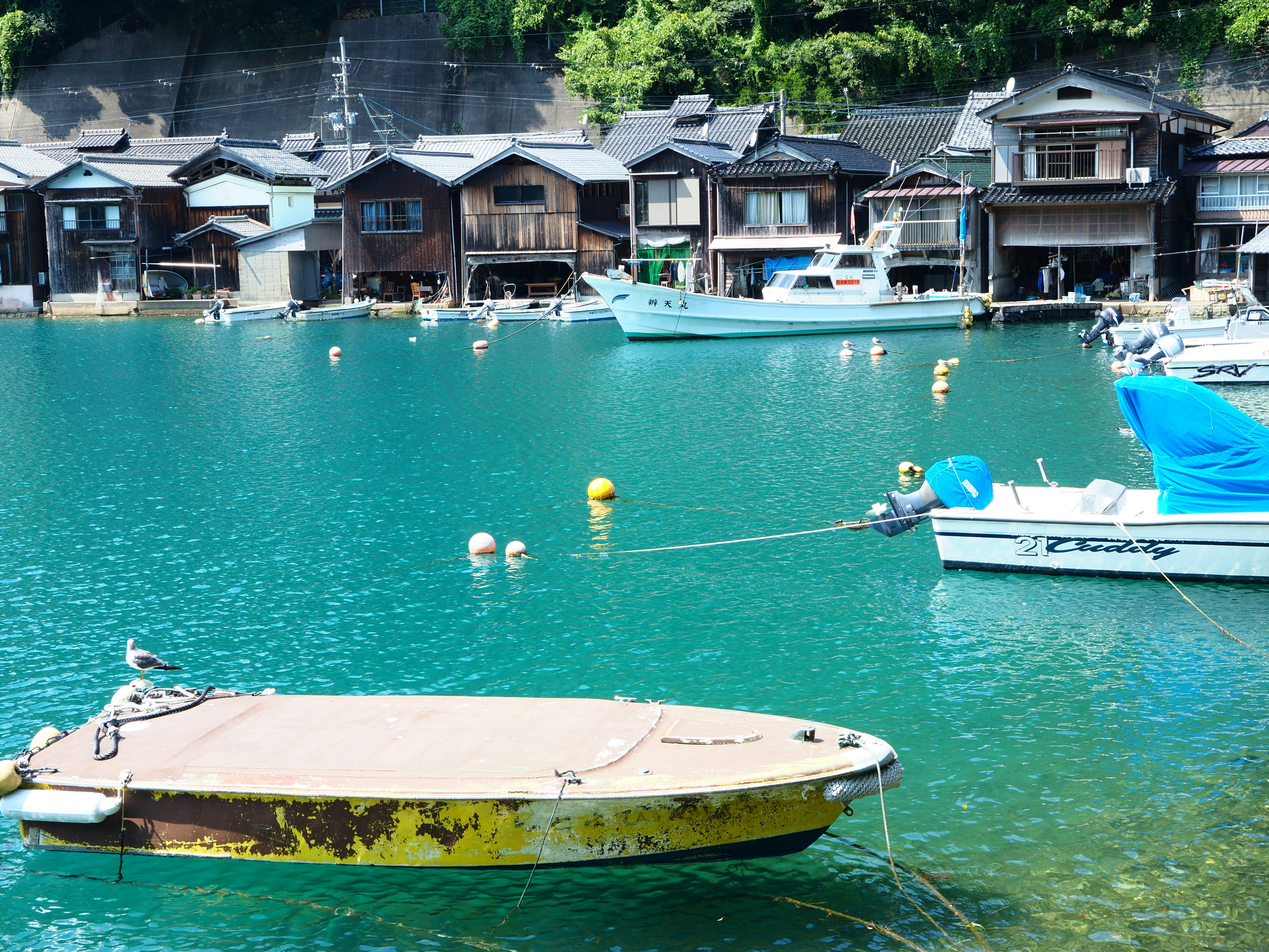 青い水面に浮かぶ小舟と伝統的な漁村の家々が並ぶ風景