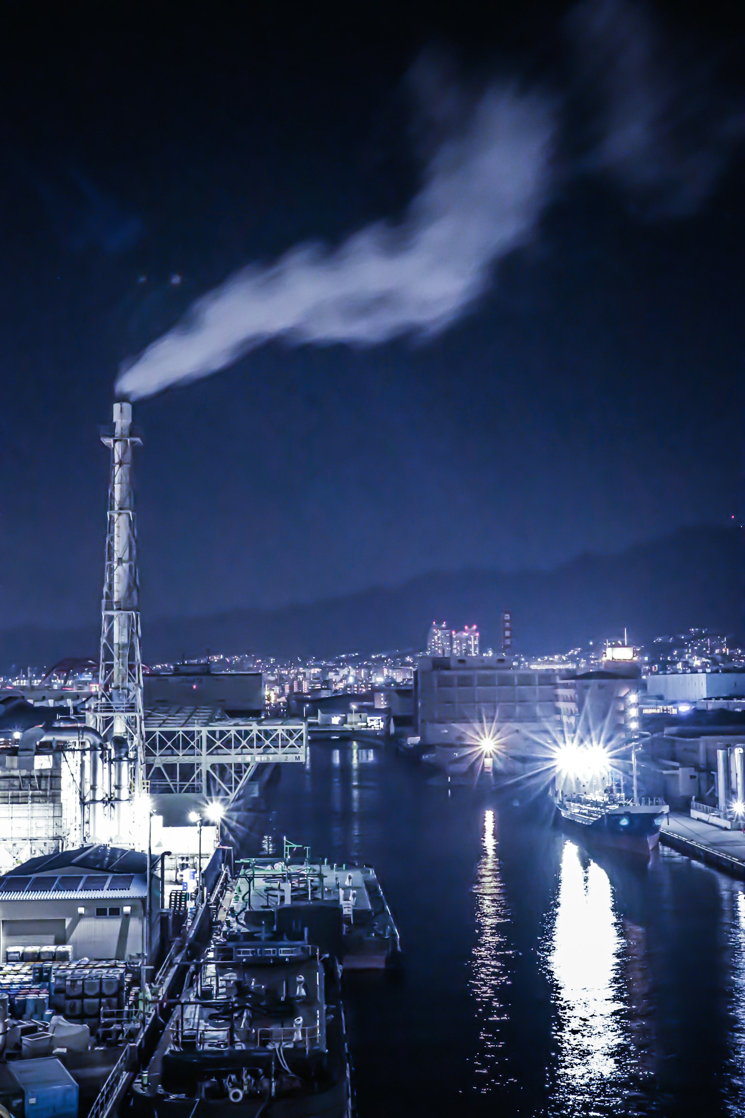 Nighttime industrial landscape with smoke rising from a chimney over the harbor