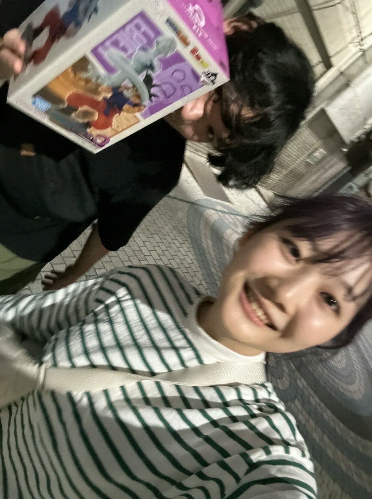 两位女性在夜间环境中自拍，一位手持彩色盒子