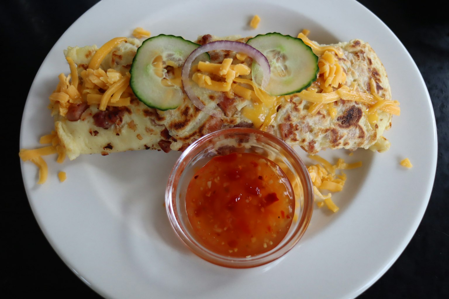 Omelet yang dihiasi keju dan mentimun disajikan dengan saus cabai manis