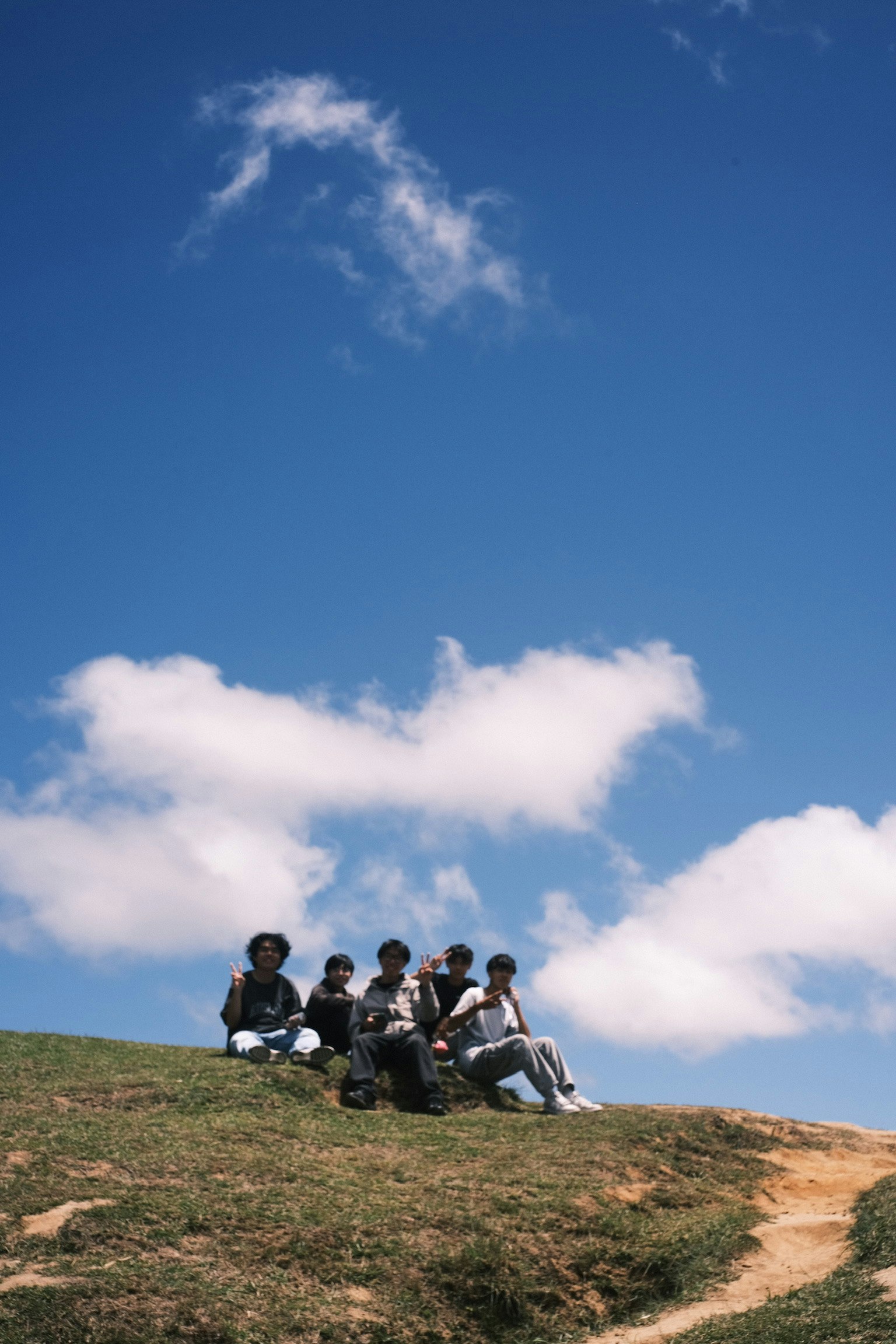 Five people sitting on a grassy hill under a blue sky