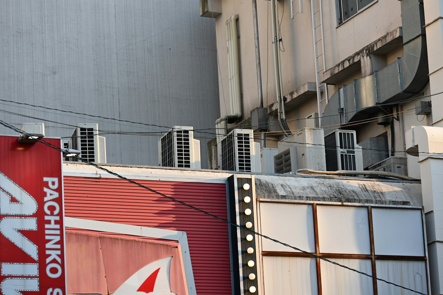 Esquina de un edificio con un letrero de pachinko y múltiples unidades de aire acondicionado