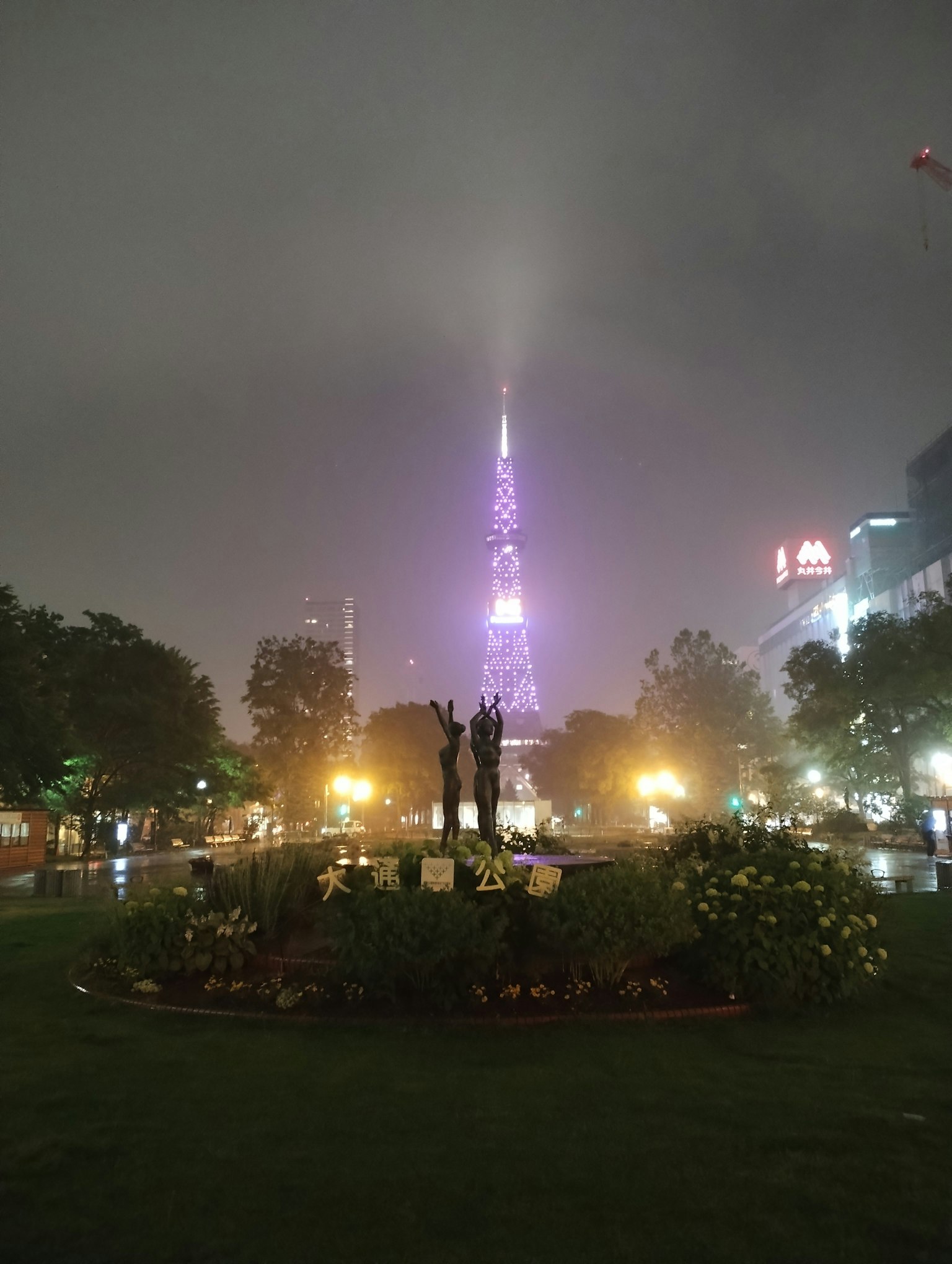 Statue dans un parc nocturne avec une tour violette brillant dans le brouillard