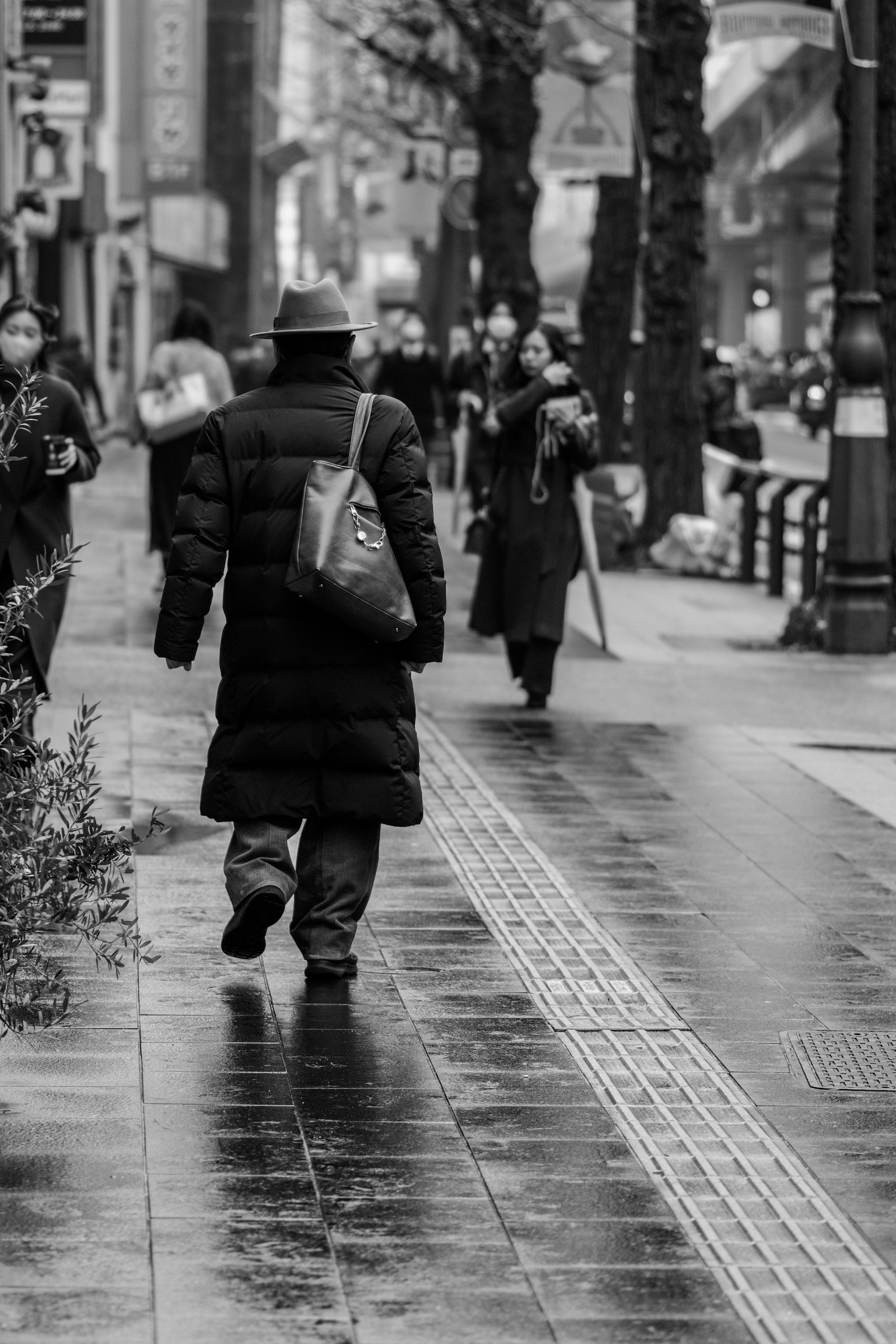 Schwarz-Weiß-Straßenszene mit Menschen, die gehen, und nassem Gehweg