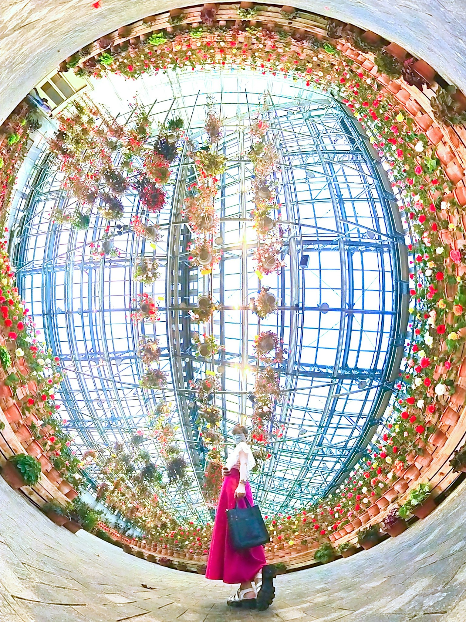Une femme en robe rouge se tient à l'intérieur d'une serre en verre ornée de fleurs suspendues colorées