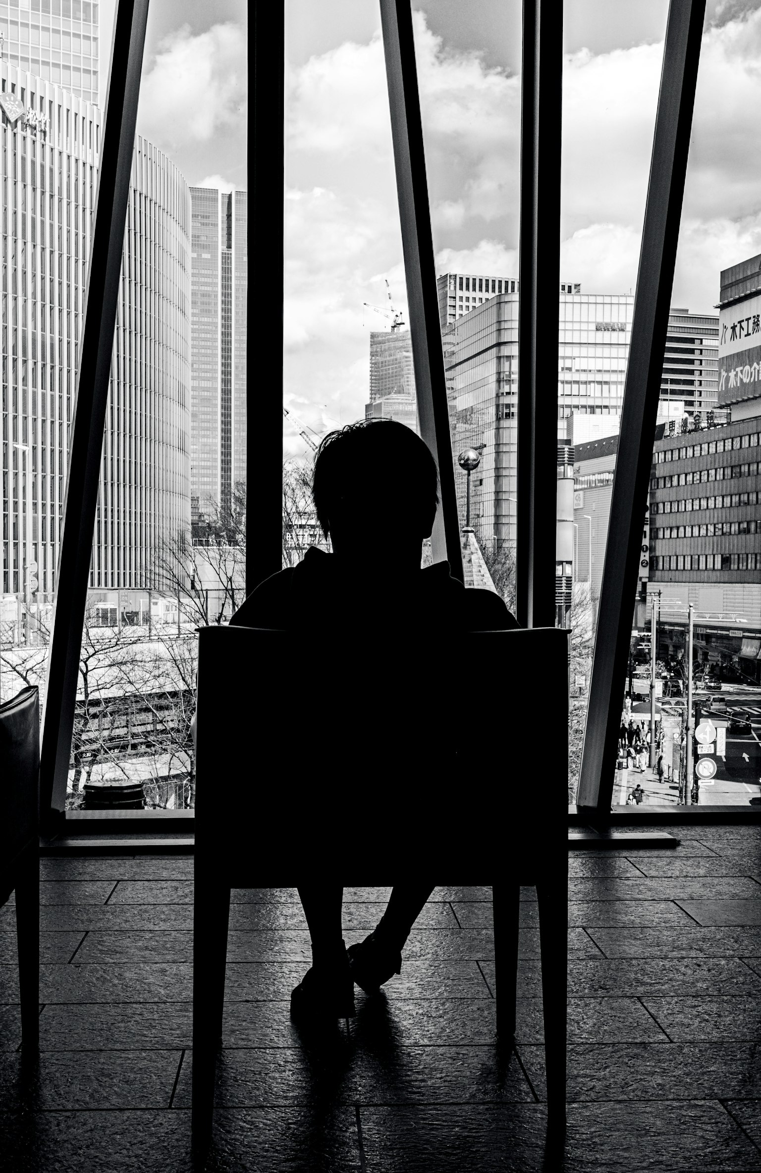 Schatten einer Person, die in einem Stuhl sitzt, mit einer Stadtlandschaft, die durch große Fenster sichtbar ist