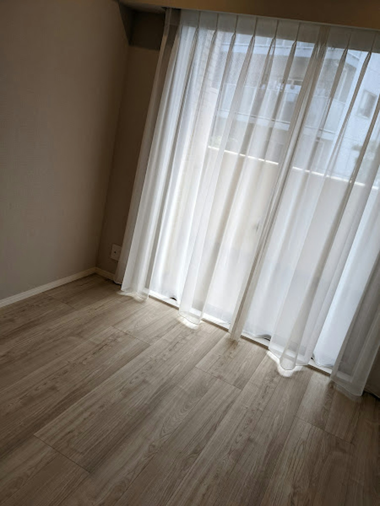 Ecke eines Raumes mit hellem Boden und durchsichtigen Vorhängen