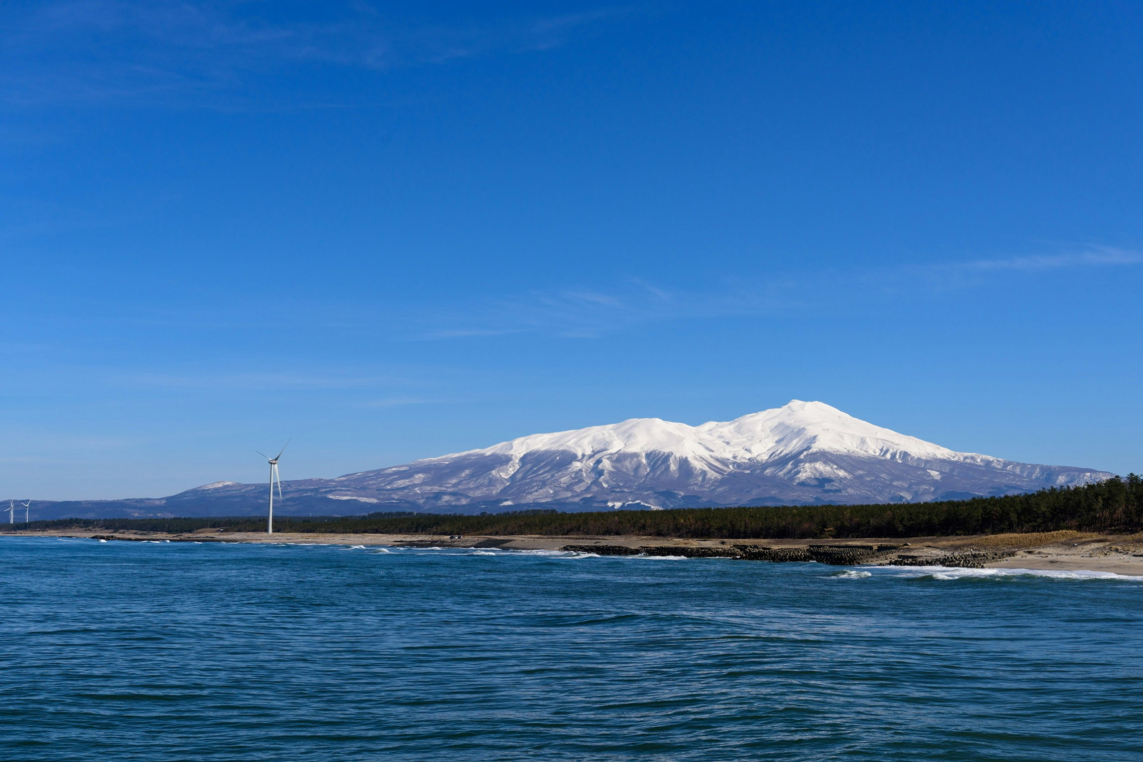 青空の下、海原と鳥海山を望む冬の風景
