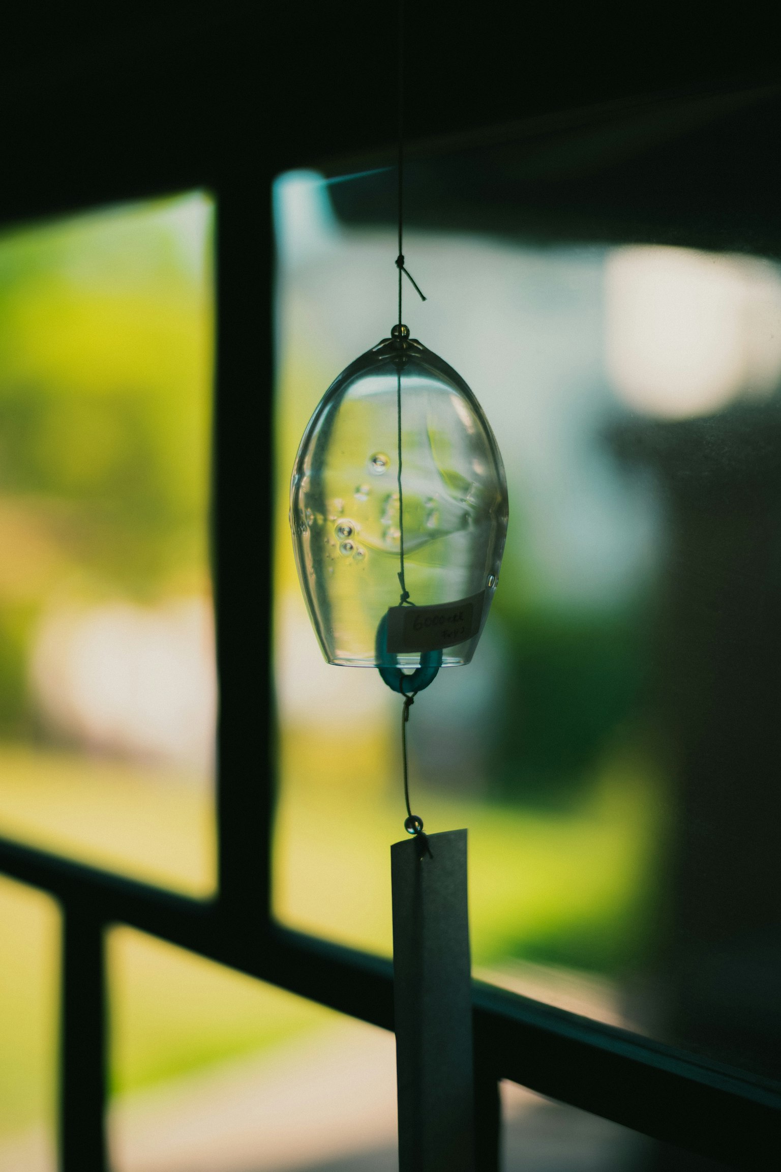 透明な風鈴が窓辺にぶら下がっている背景に緑の風景
