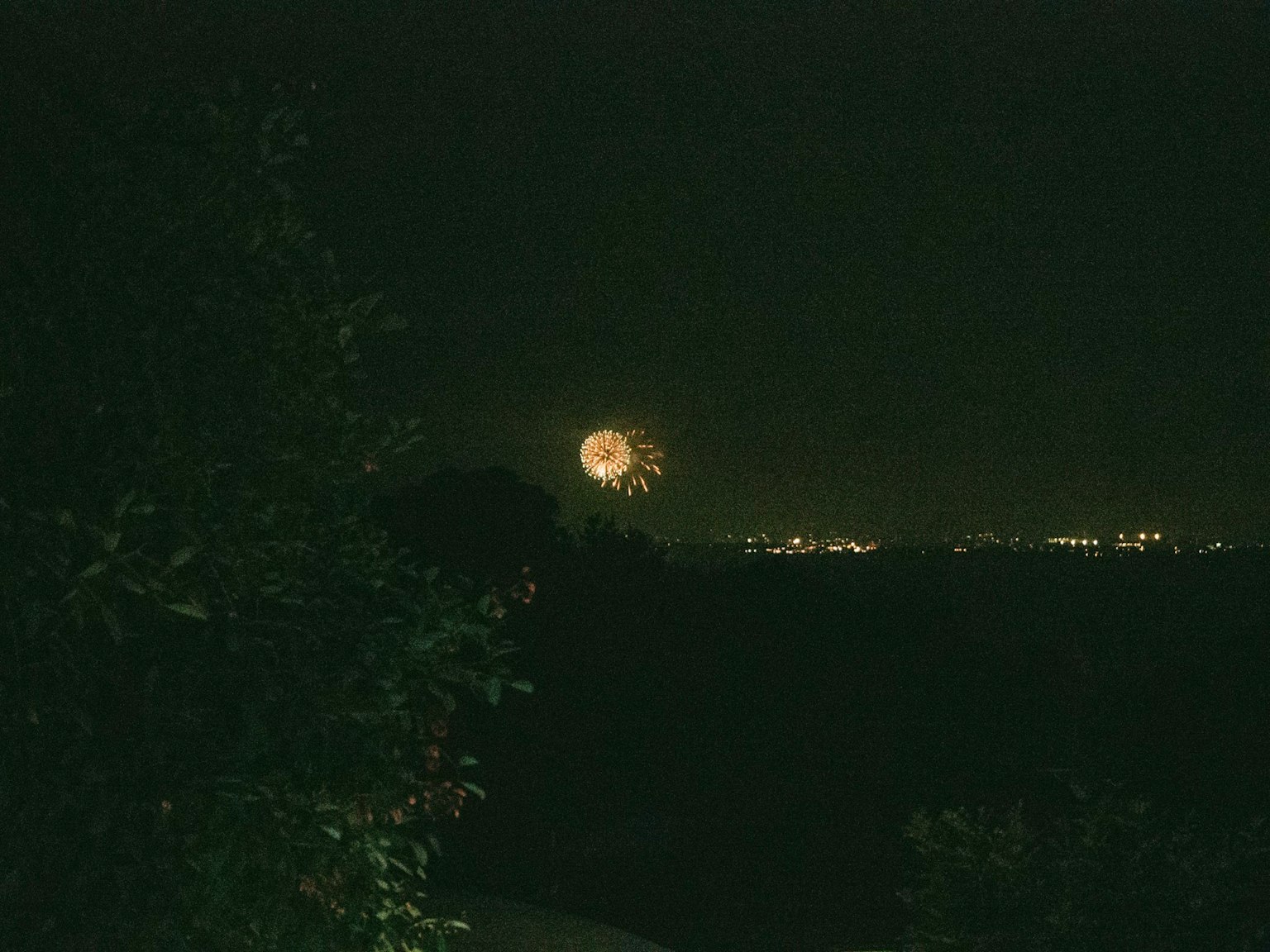 Una luna grande ascendiendo en un cielo nocturno oscuro con fuegos artificiales a lo lejos