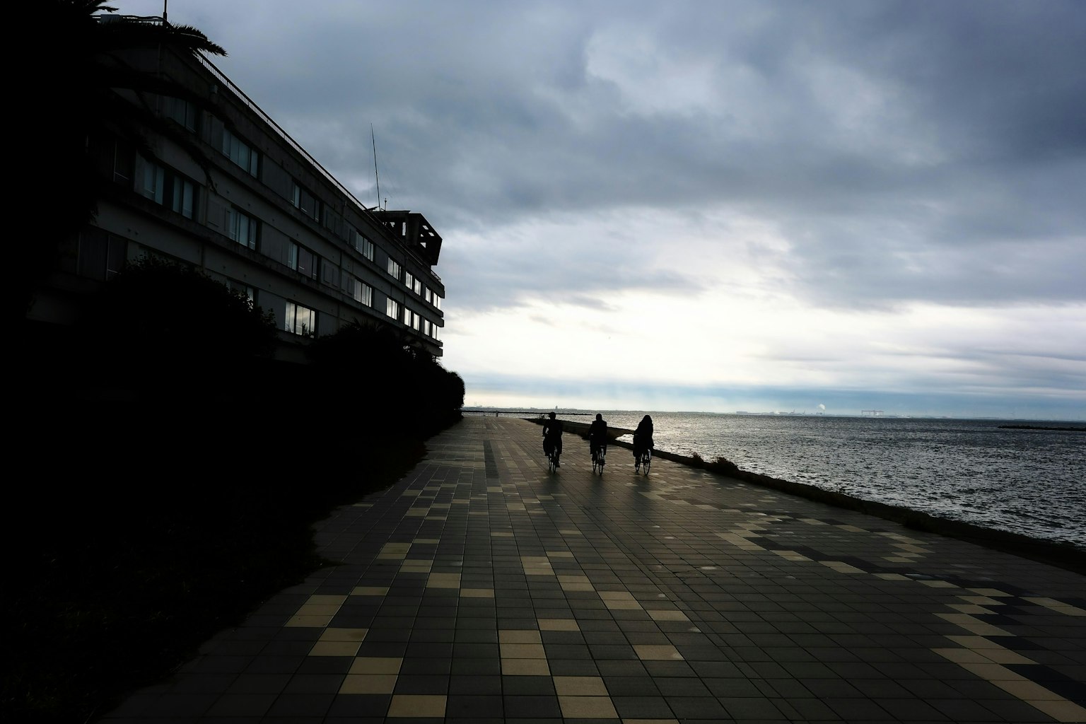 Silhouette di persone che camminano lungo un sentiero costiero sotto un cielo nuvoloso