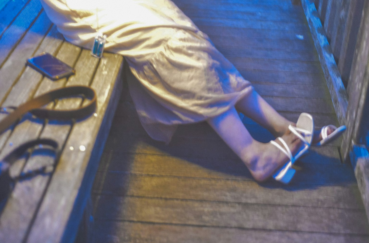 A woman's feet in white sandals resting on a wooden bench under blue lighting