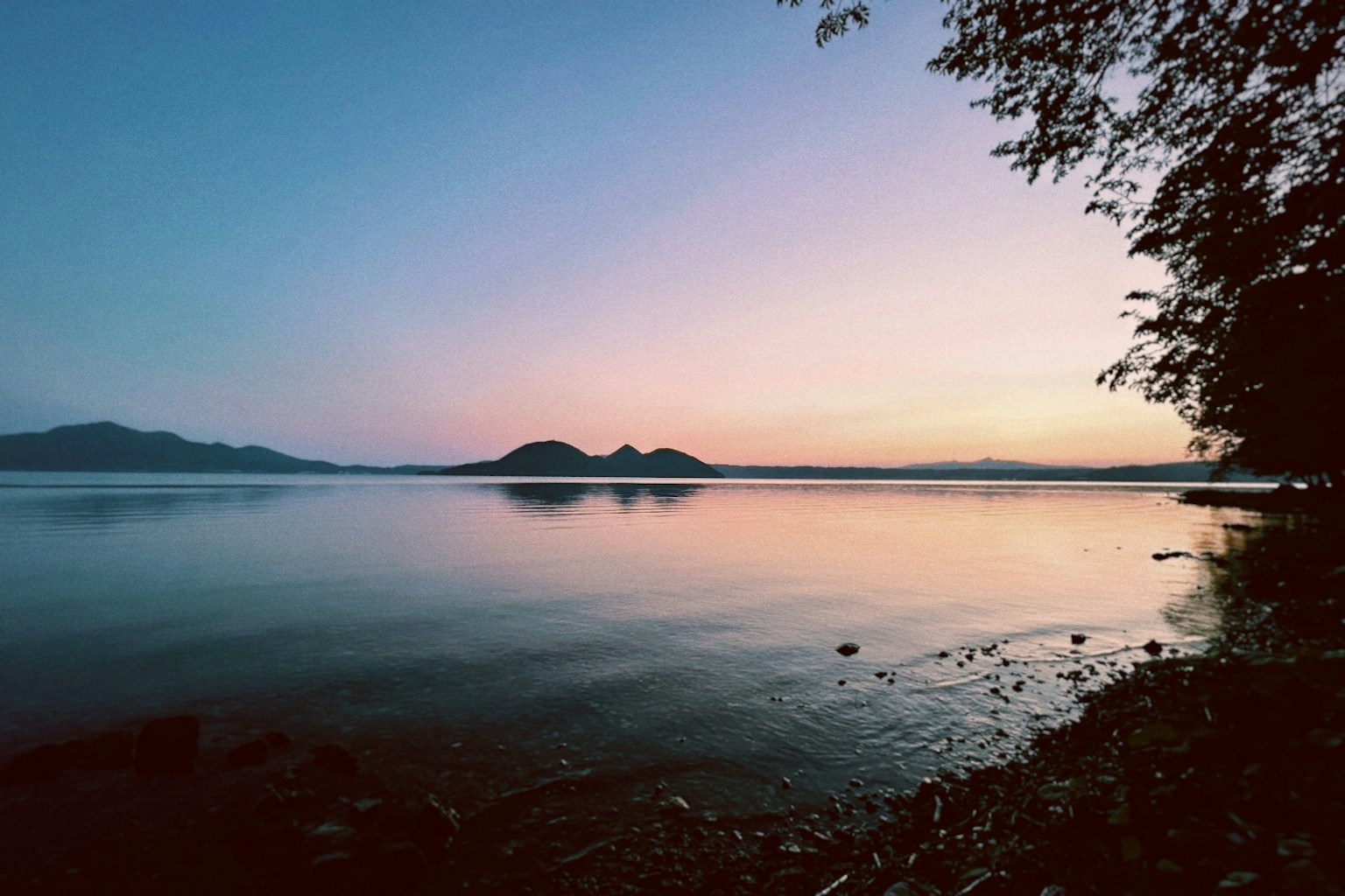 Ruhiger See bei Sonnenuntergang mit Bergen, die sich im Wasser spiegeln und einem Farbverlauf