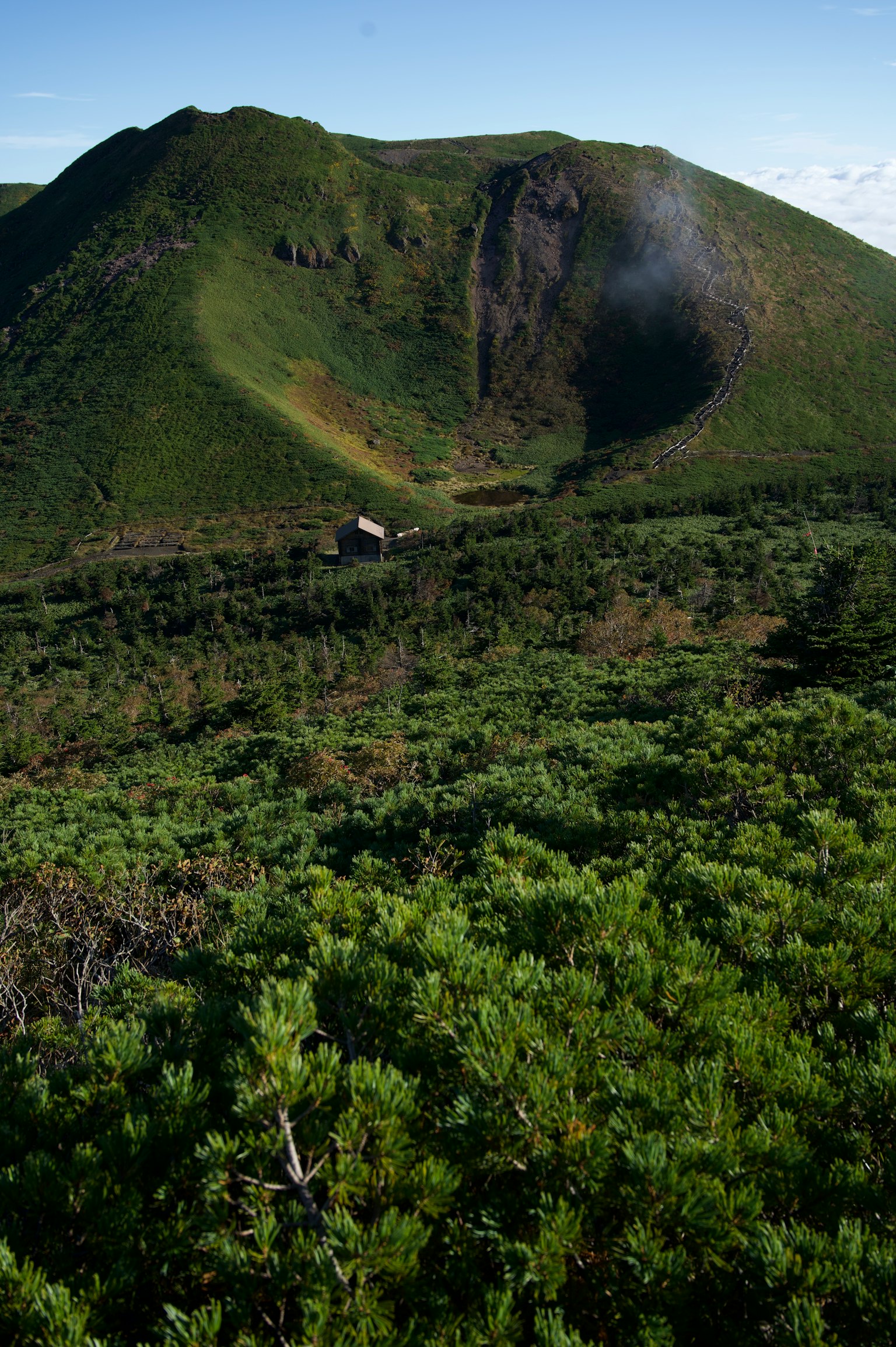 Vulkanlandschaft umgeben von grüner Vegetation und einer kleinen Hütte