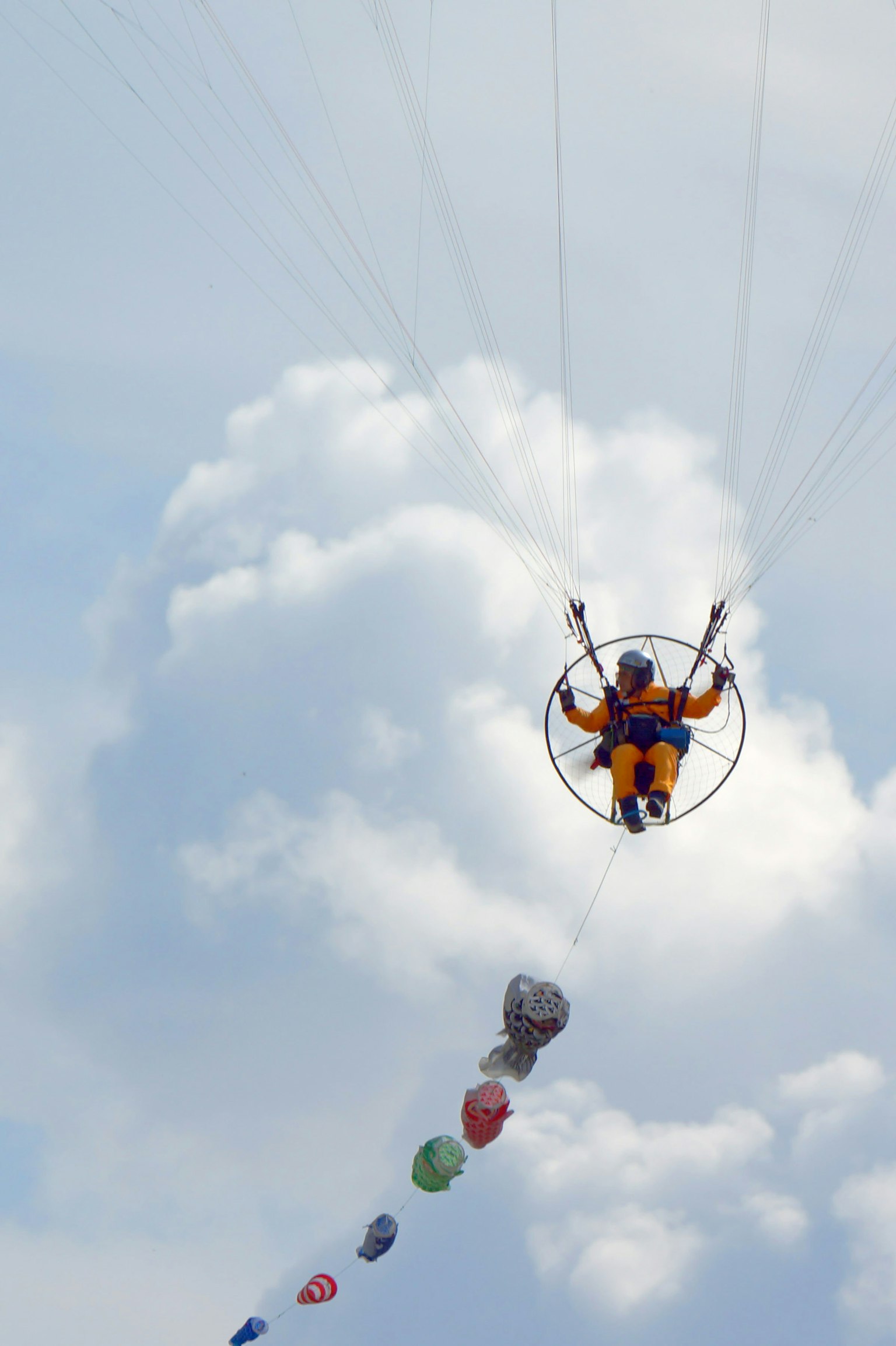 Orang yang menikmati paralayang di langit biru dengan awan mengenakan pakaian oranye dan bingkai lingkaran