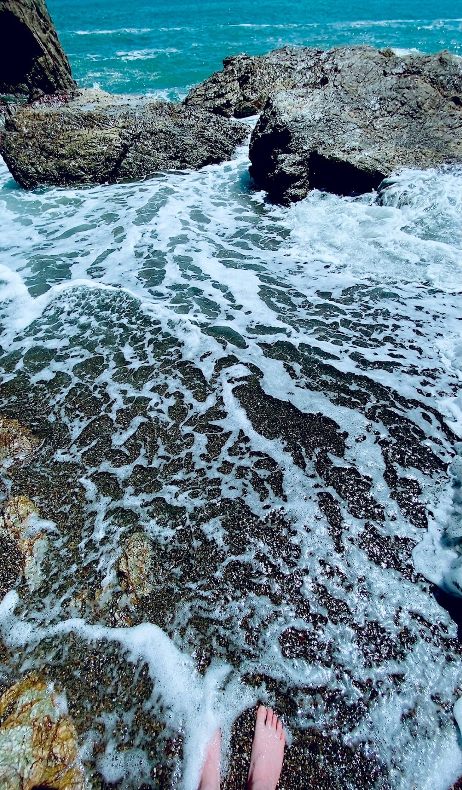 海浪拍打岩石，脚在浅水中