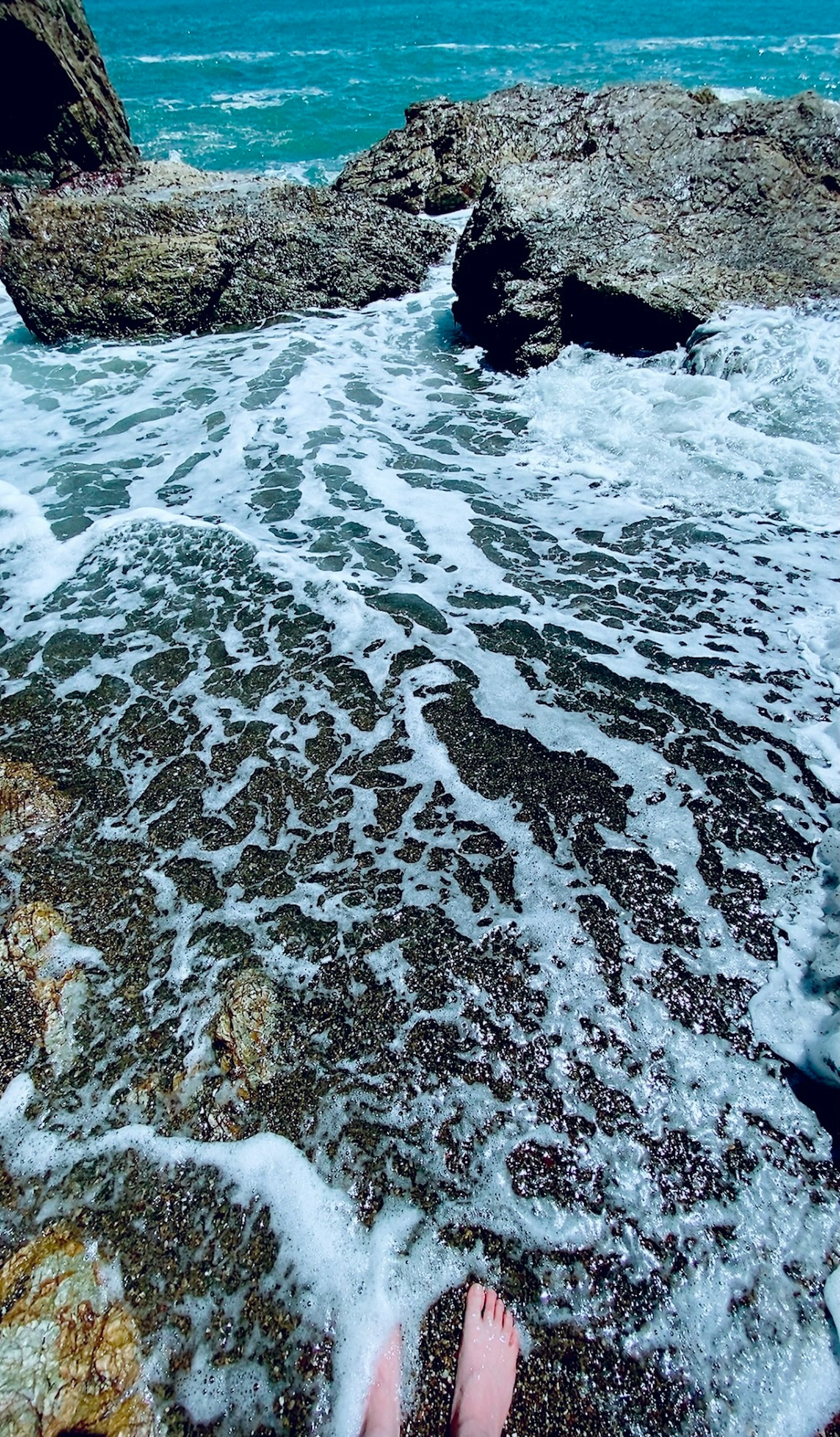 Onde che si infrangono su rocce con piedi nell'acqua bassa