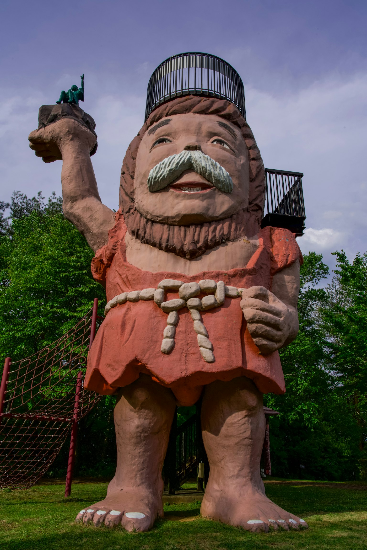 一個巨大的男人雕像在綠色公園中舉著一個小雕像