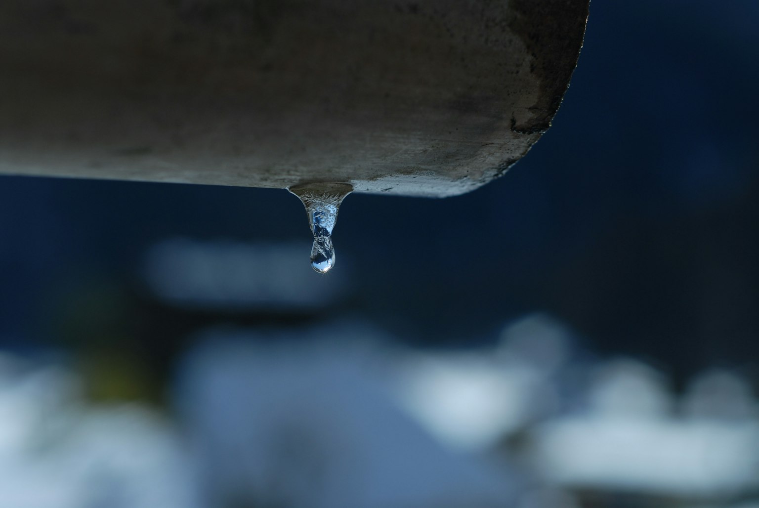 Wassertropfen hängt von einem Rohr mit verschwommenem Hintergrund