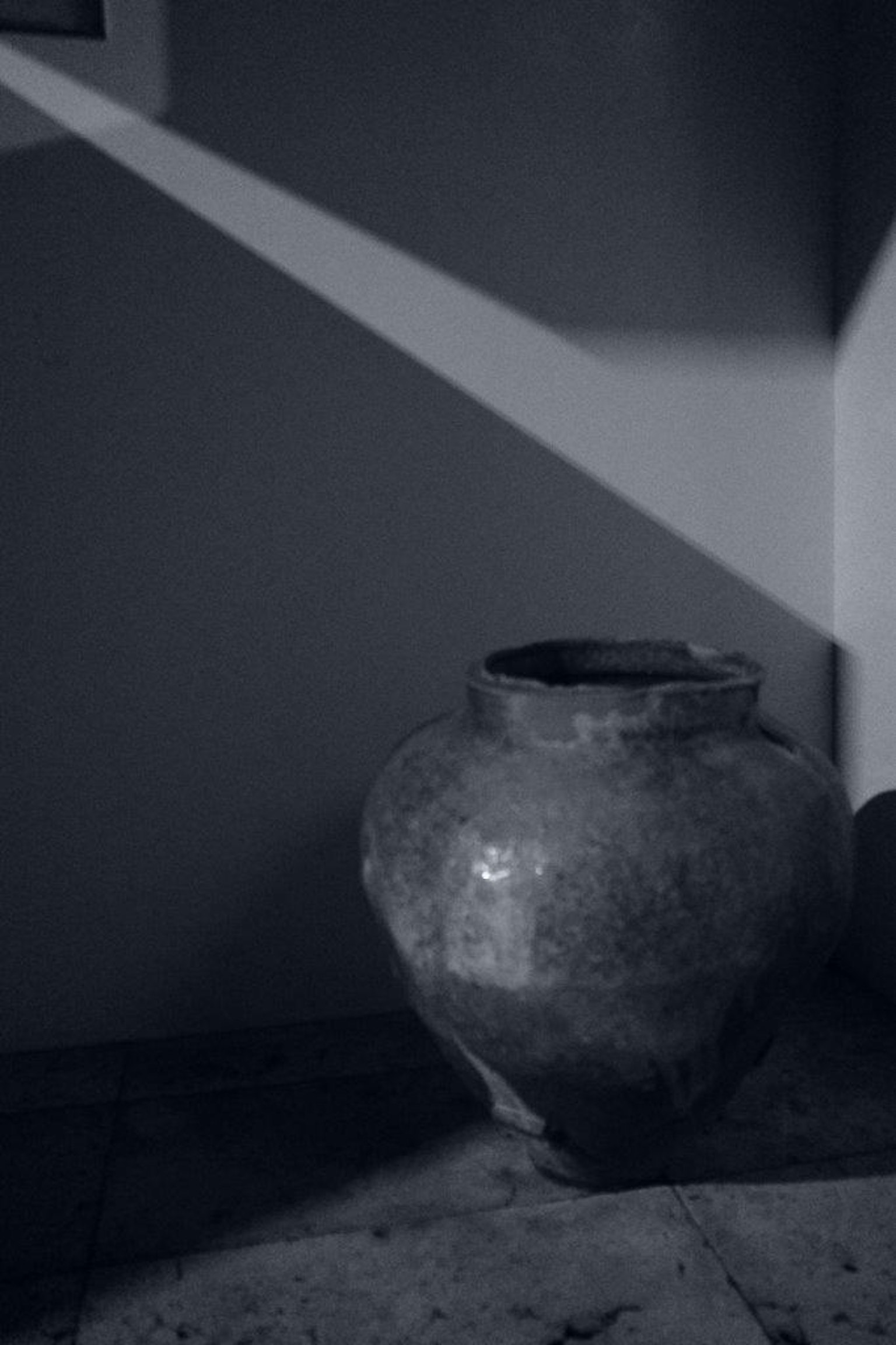 Un pot en céramique placé contre un fond sombre illuminé par une lumière diagonale