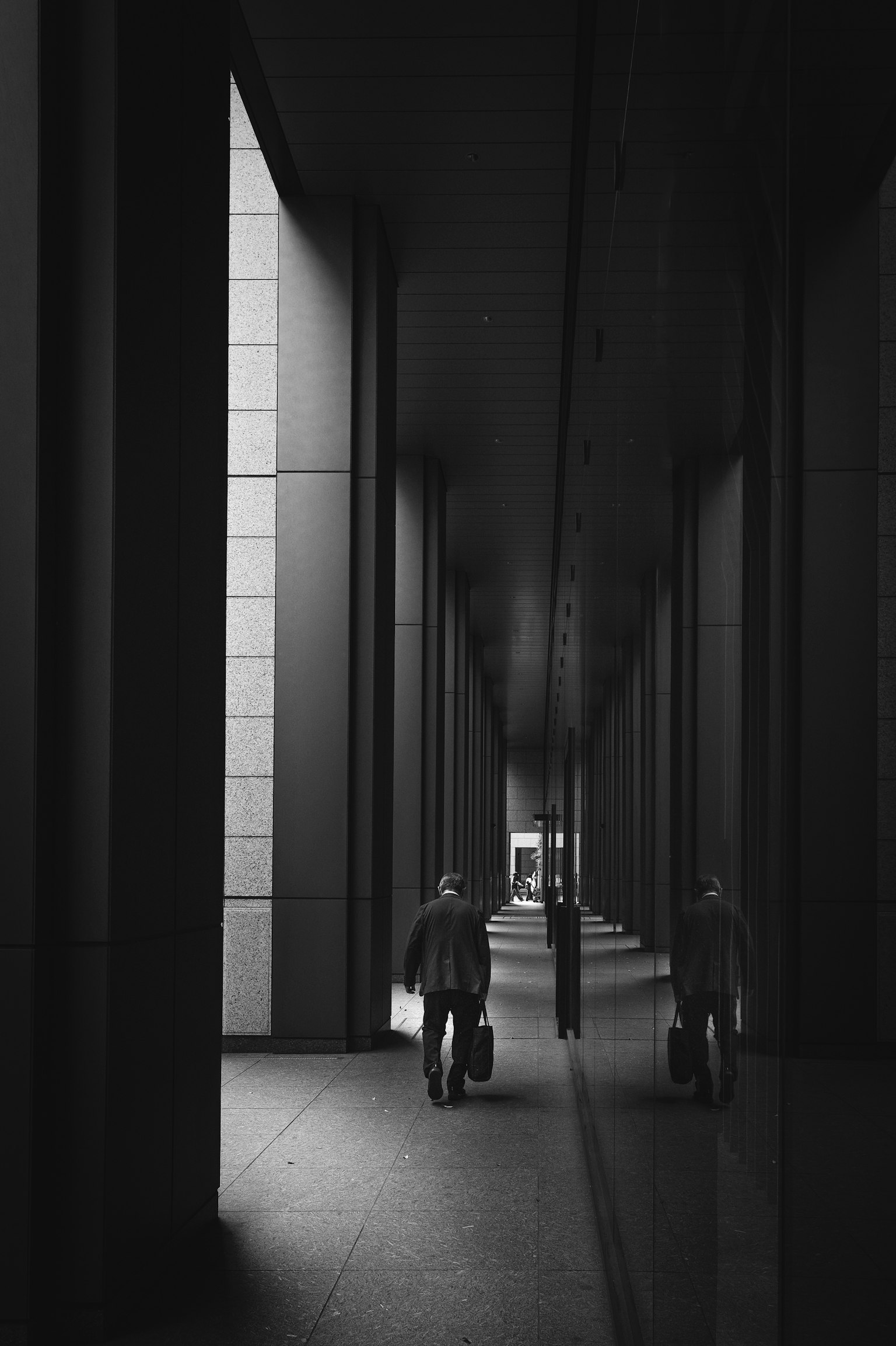 Monochrome photo of a person walking through a dark corridor with reflections