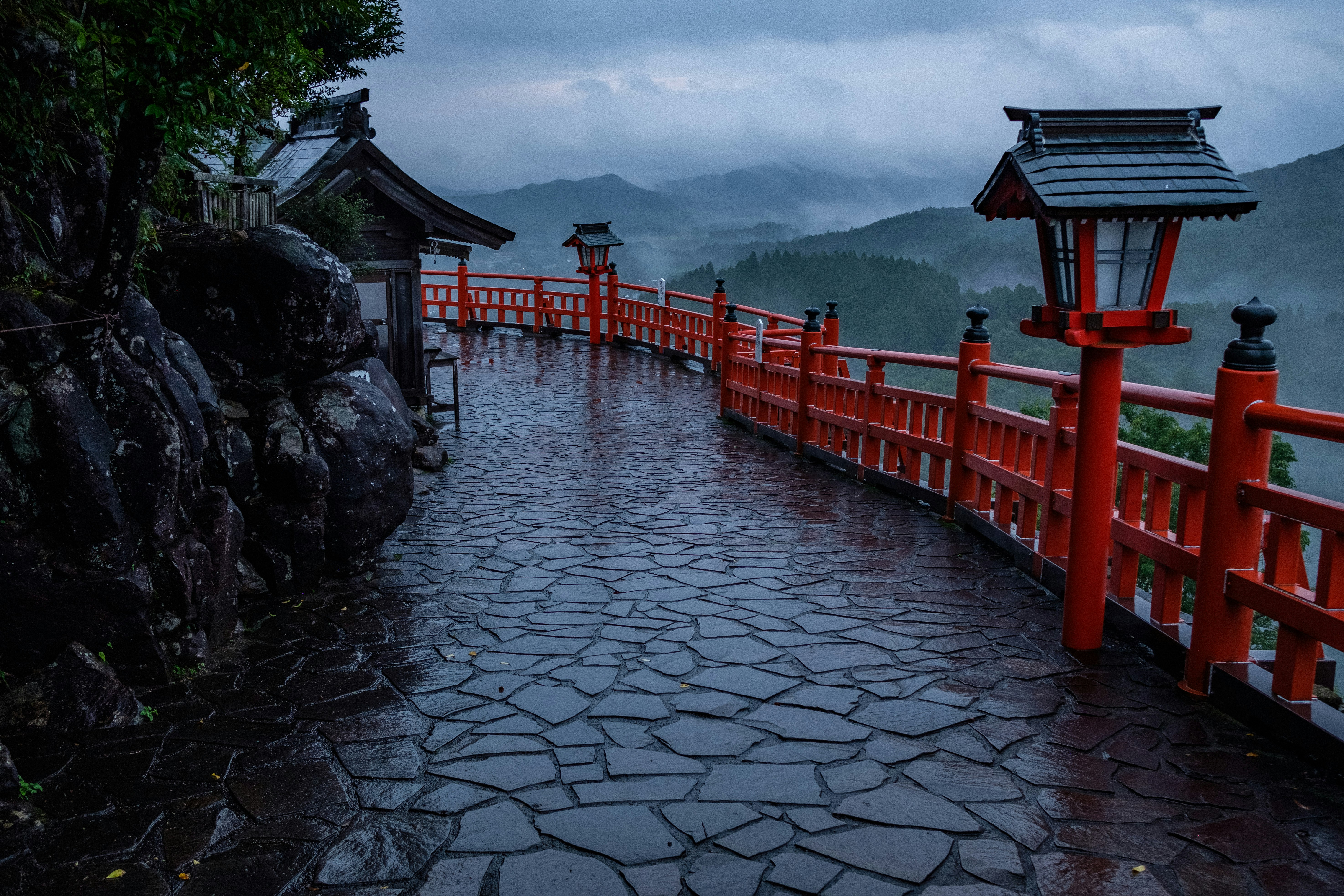 雨の中の朱塗りの鳥居と石畳の参道、霞神社