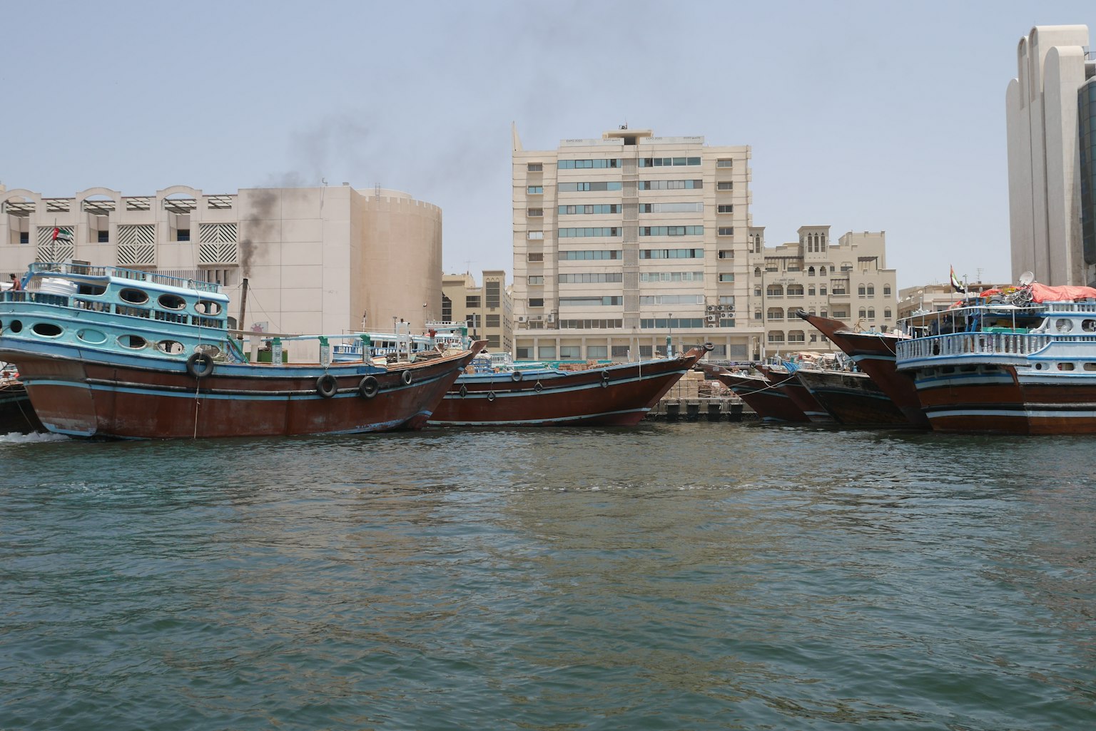 Perahu Arab tradisional berlabuh di air dengan bangunan modern di latar belakang