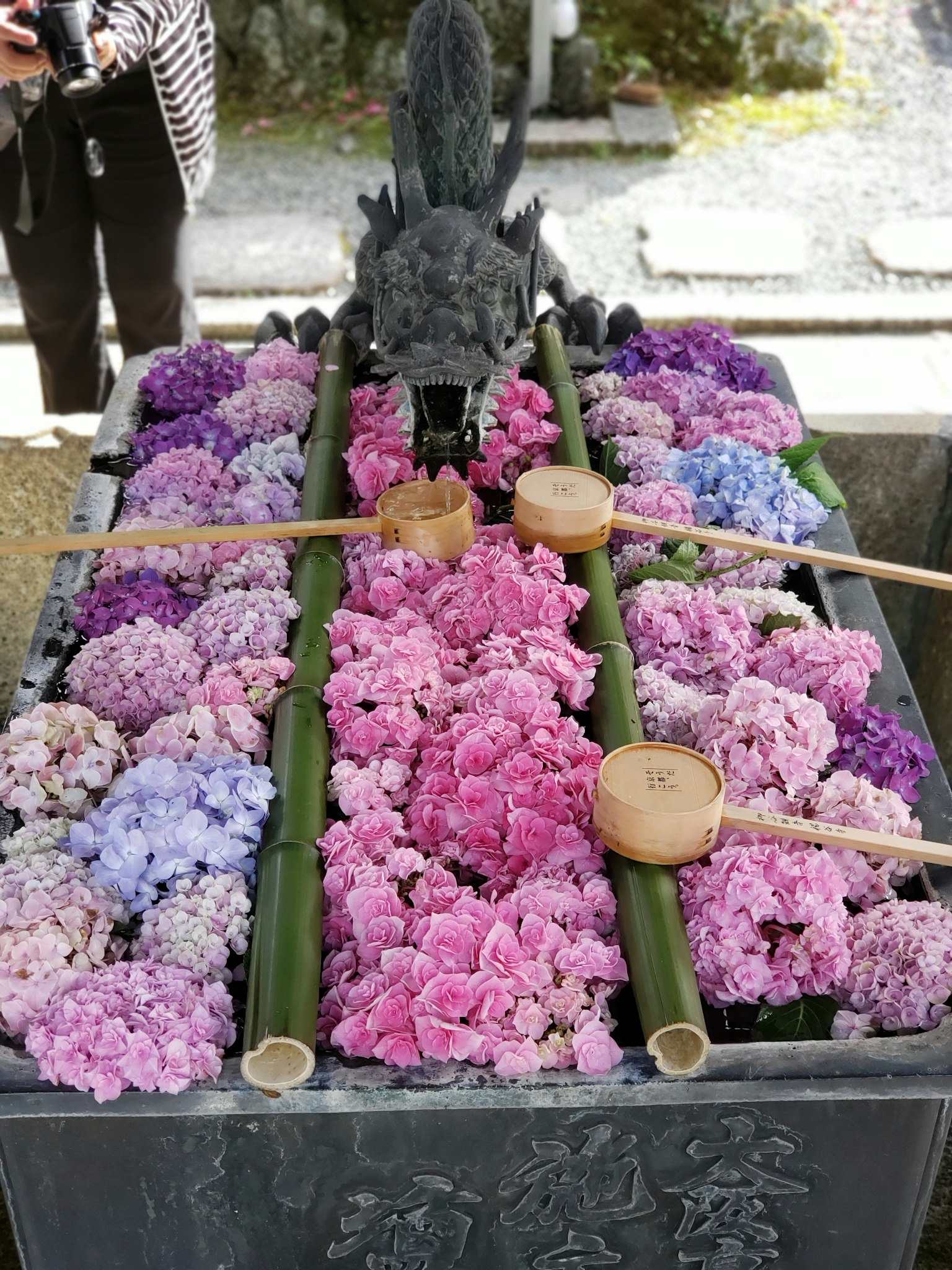 A stone basin filled with colorful flowers and bamboo ladles at a shrine