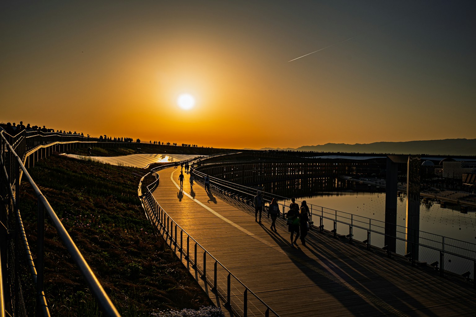 Personas caminando por un paseo junto al río al atardecer