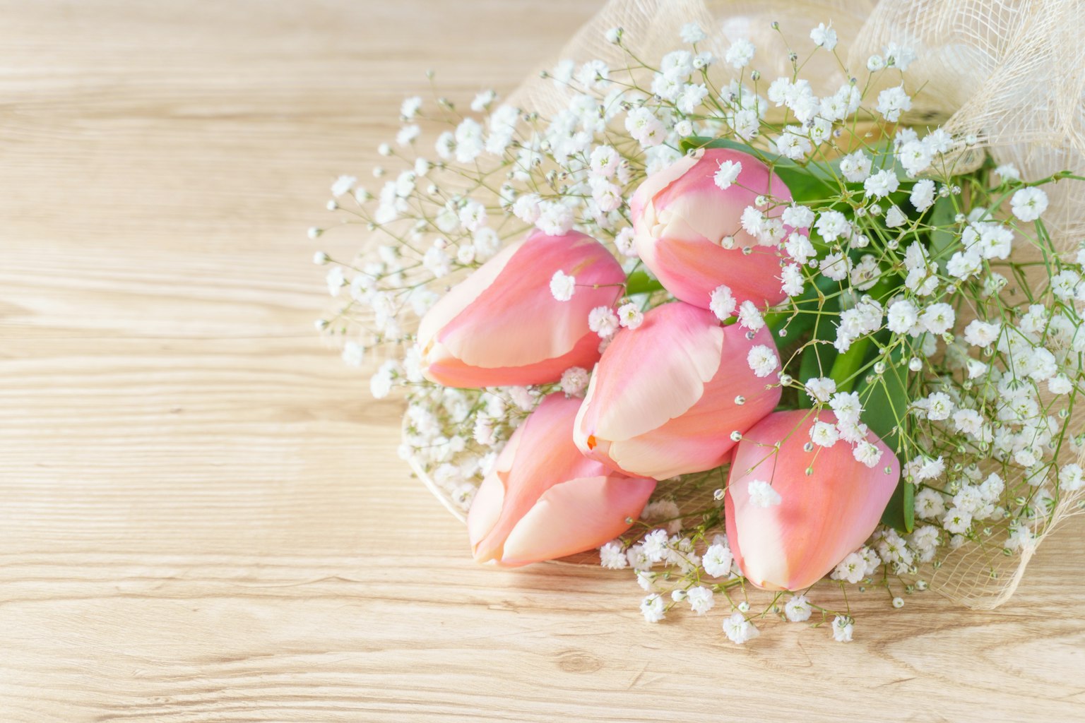 Strauß aus rosa Tulpen und Schleierkraut auf einer Holzoberfläche