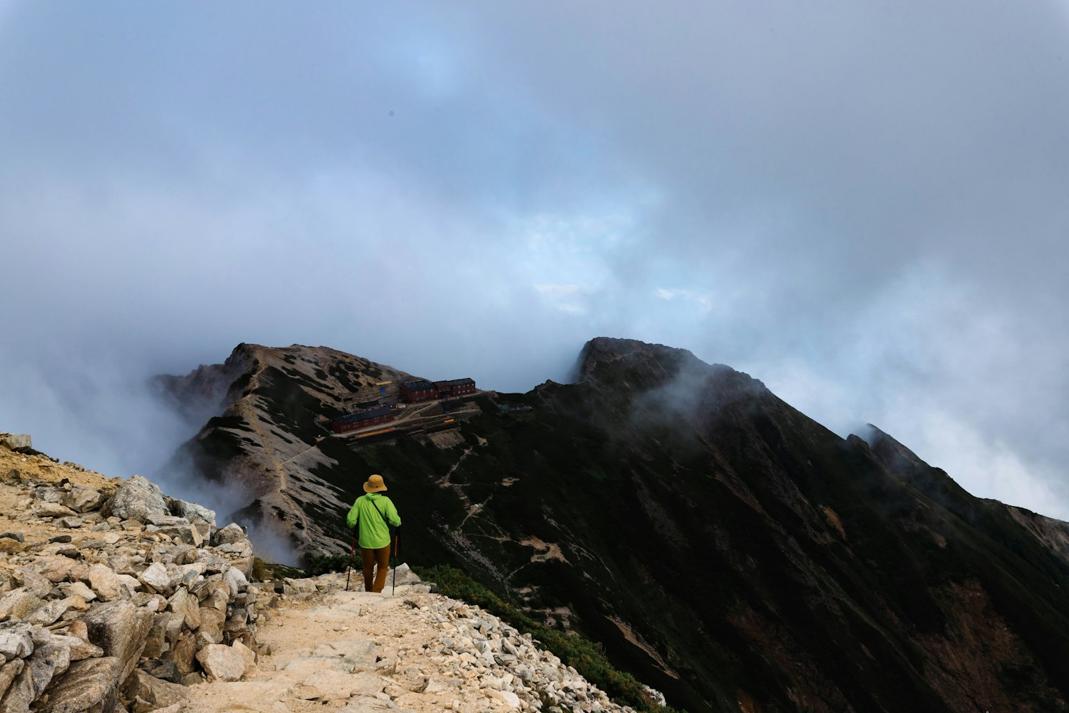 Pendaki berpakaian hijau berjalan di jalur gunung berkabut