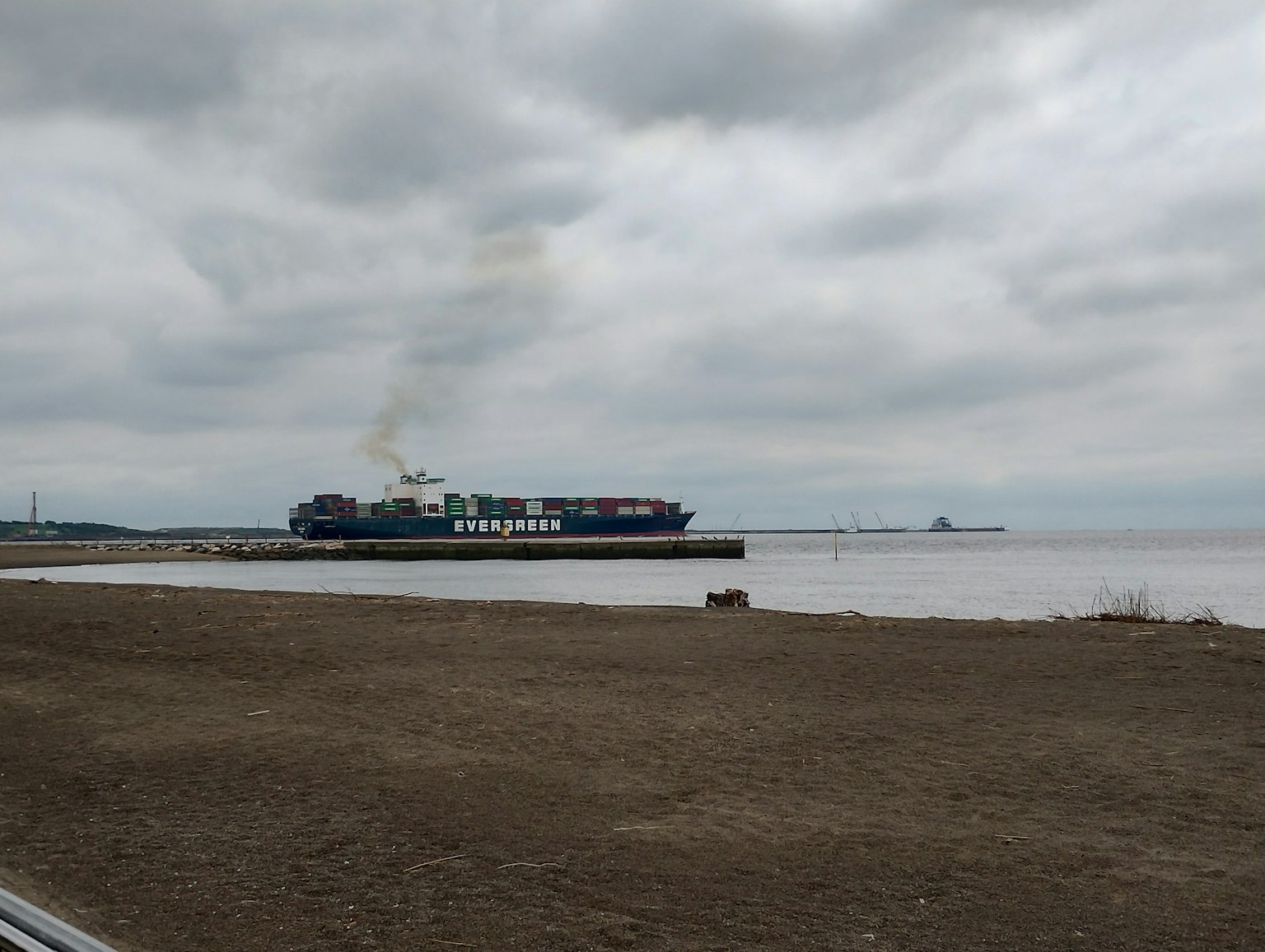 Barco de carga emitiendo humo en un día nublado cerca de la costa