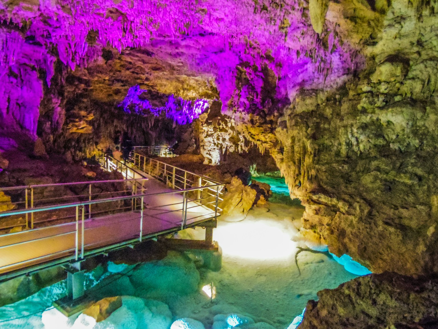Cave interior illuminated with vibrant purple lights and wooden walkway