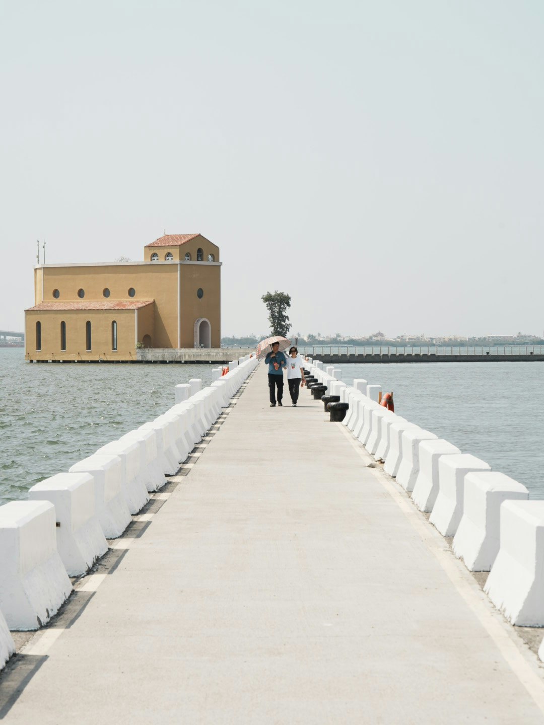 white breakwater walkway over the water with distant buildings