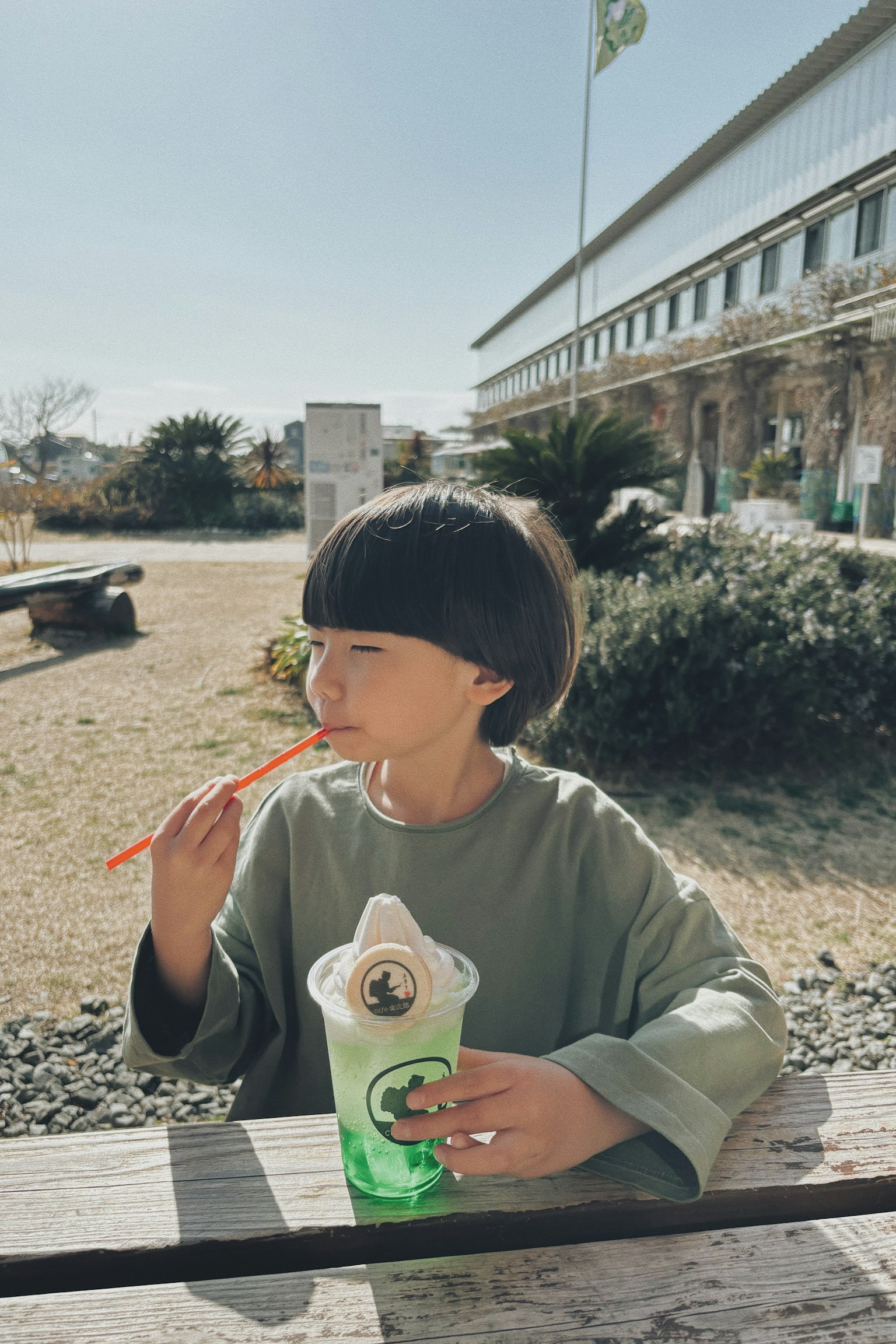 Child enjoying a green beverage with a straw on a sunny day in a park
