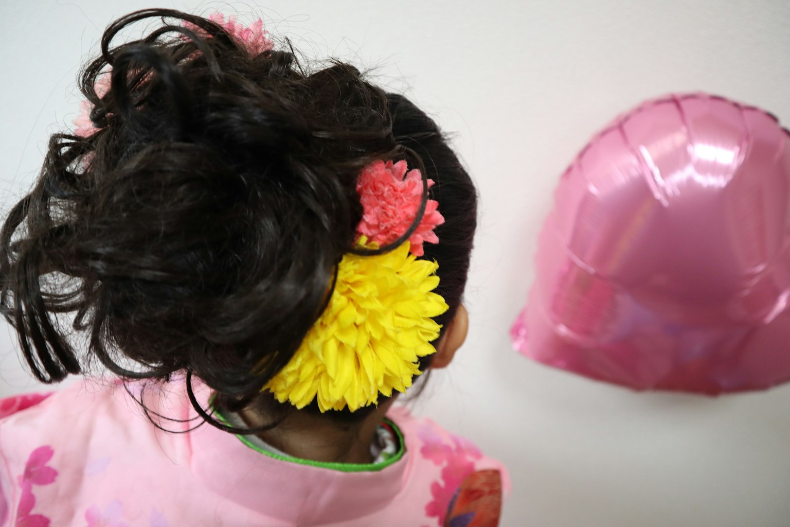 Vista posteriore di un bambino con fiori colorati nei capelli e un palloncino rosa