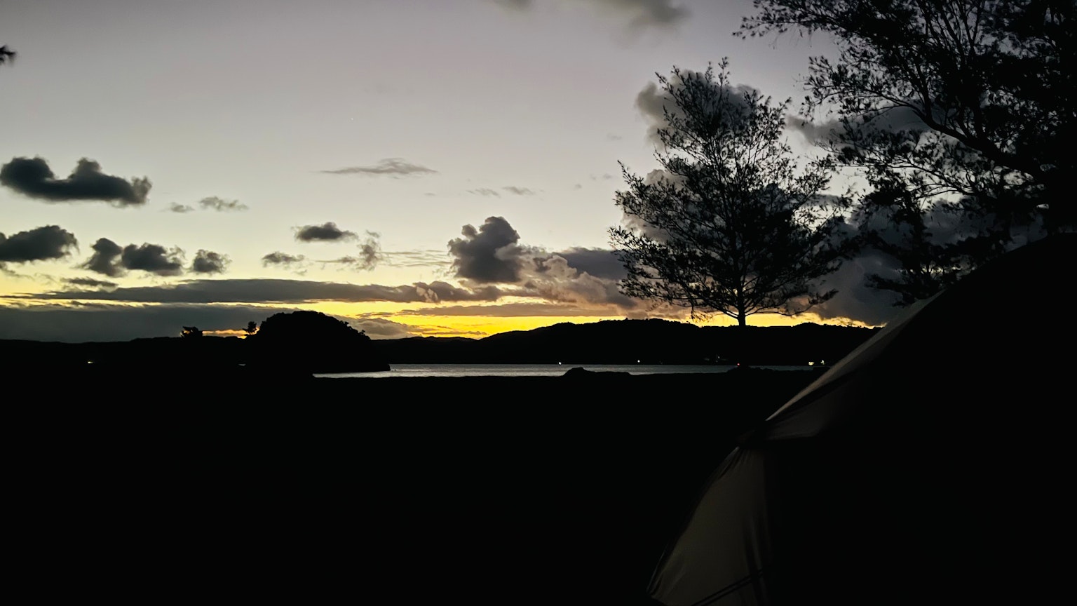 Paysage magnifique avec des silhouettes d'arbres et d'une tente le long d'une côte au coucher du soleil