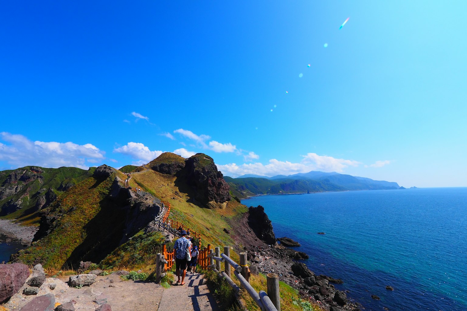Persone che camminano lungo un sentiero di montagna con uno sfondo di mare e cielo blu