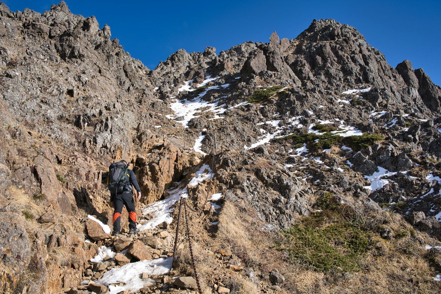 Wanderer, der felsiges Terrain mit Schneeresten erklimmt