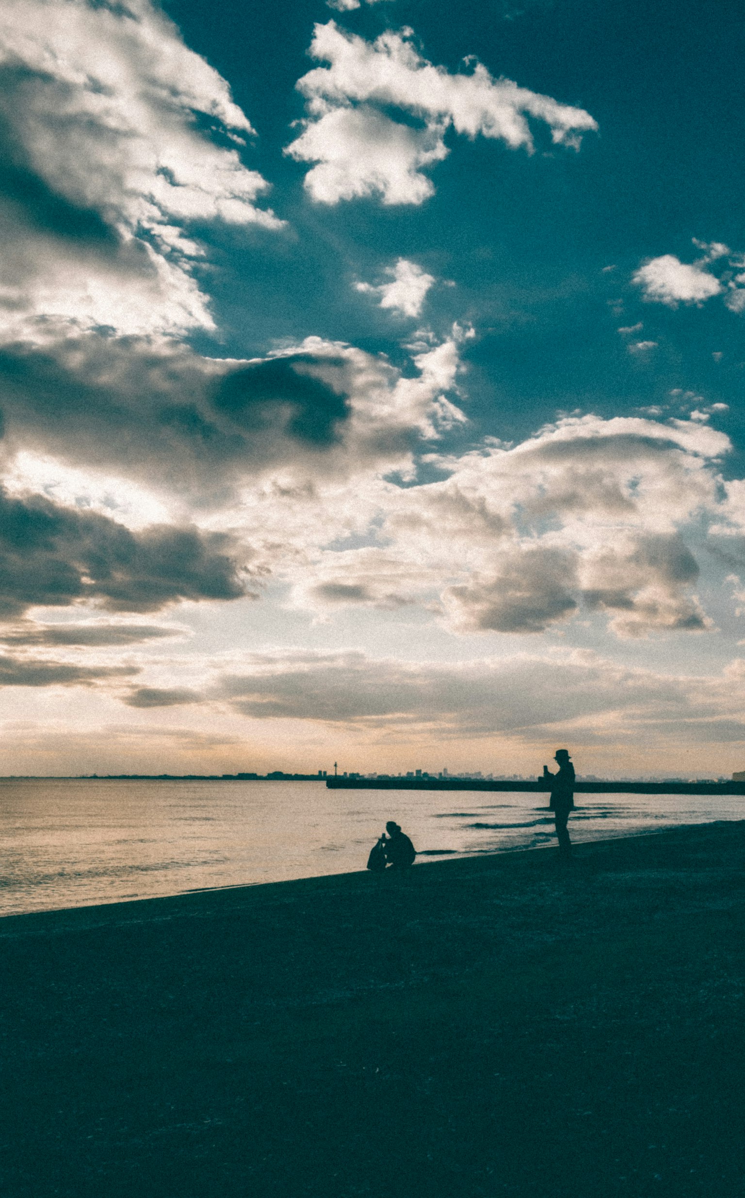 Siluet orang di pantai saat senja dengan langit berawan