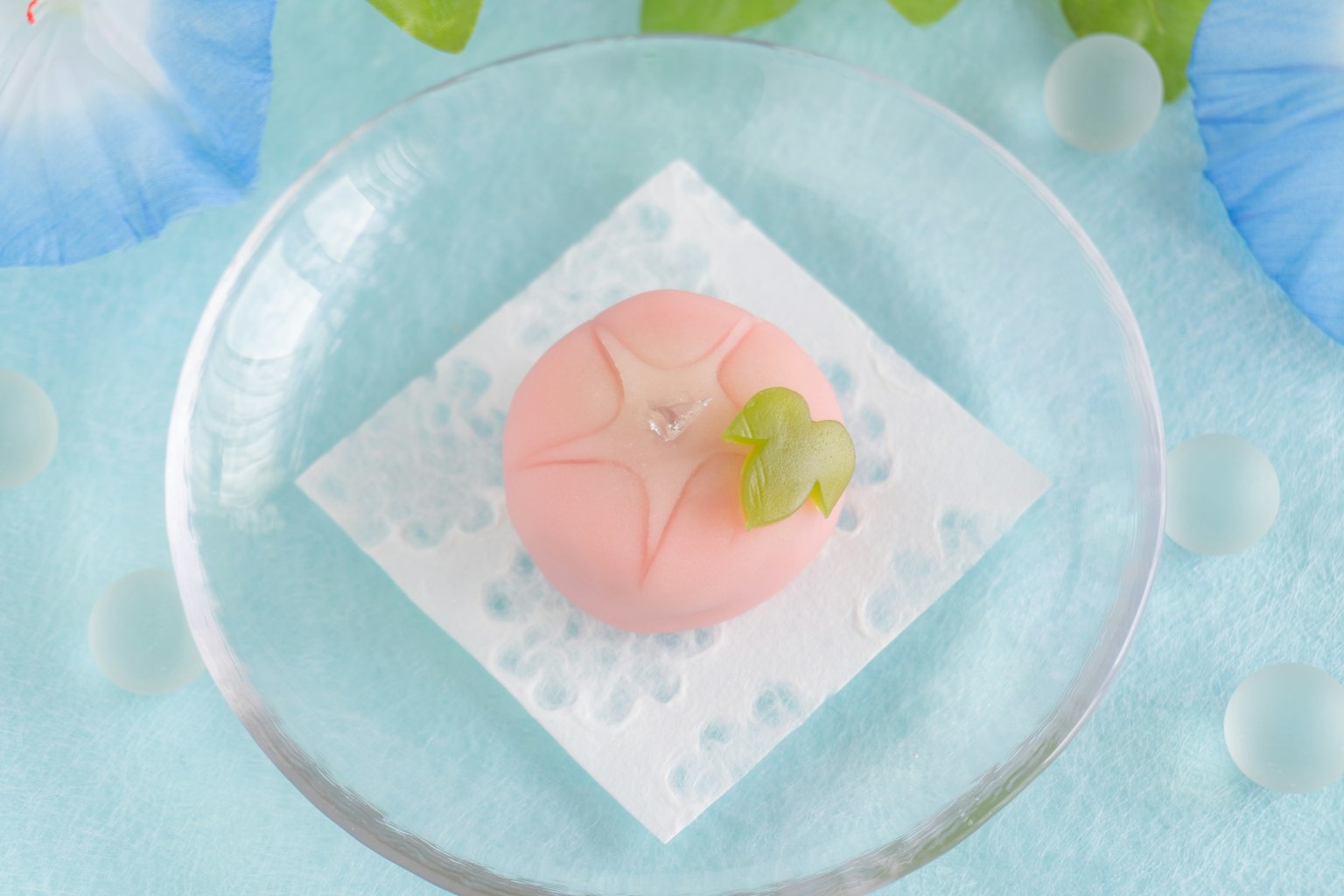 Kue Jepang berwarna merah muda di atas piring bening dengan latar belakang biru